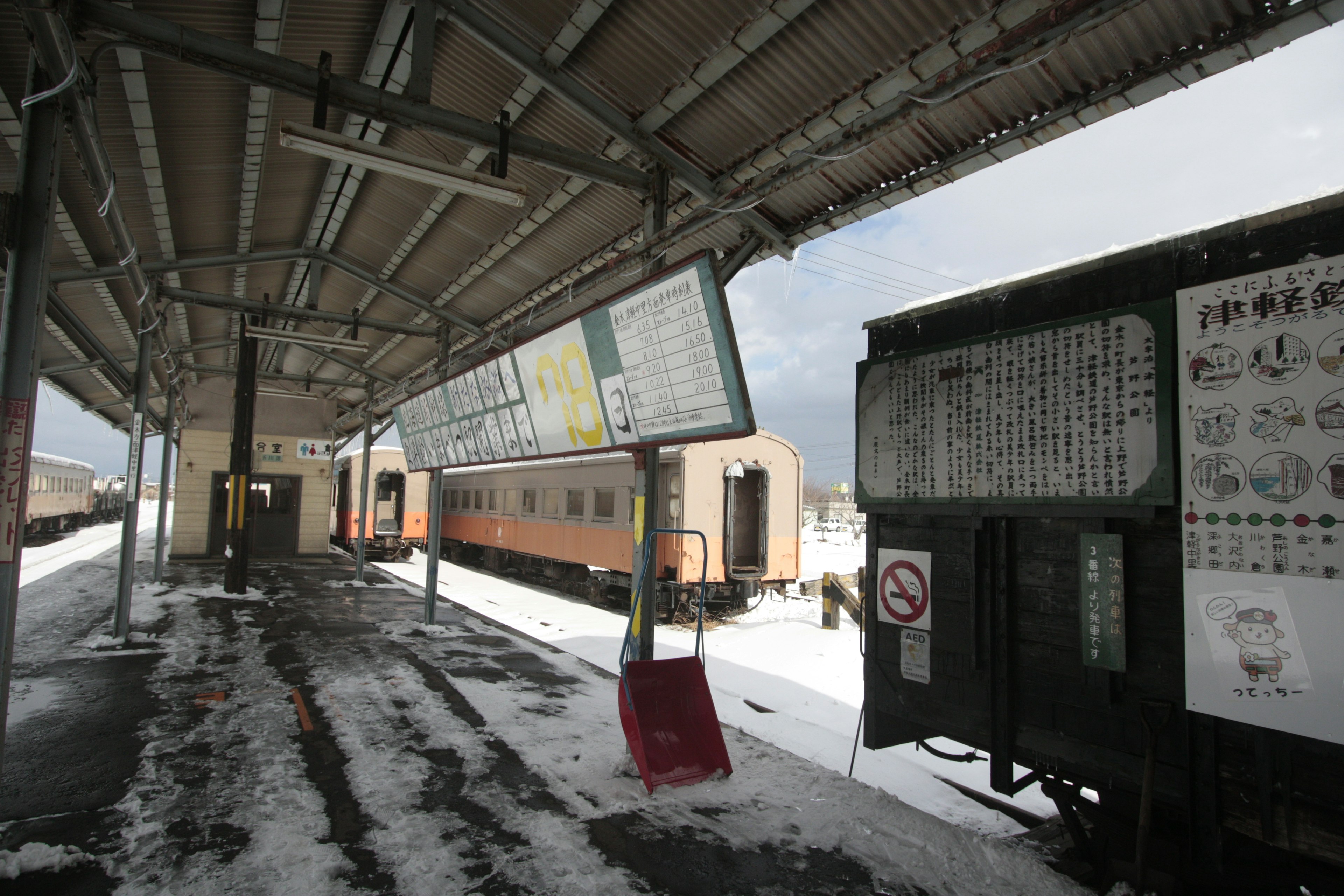 Train station covered in snow with waiting train and signboards