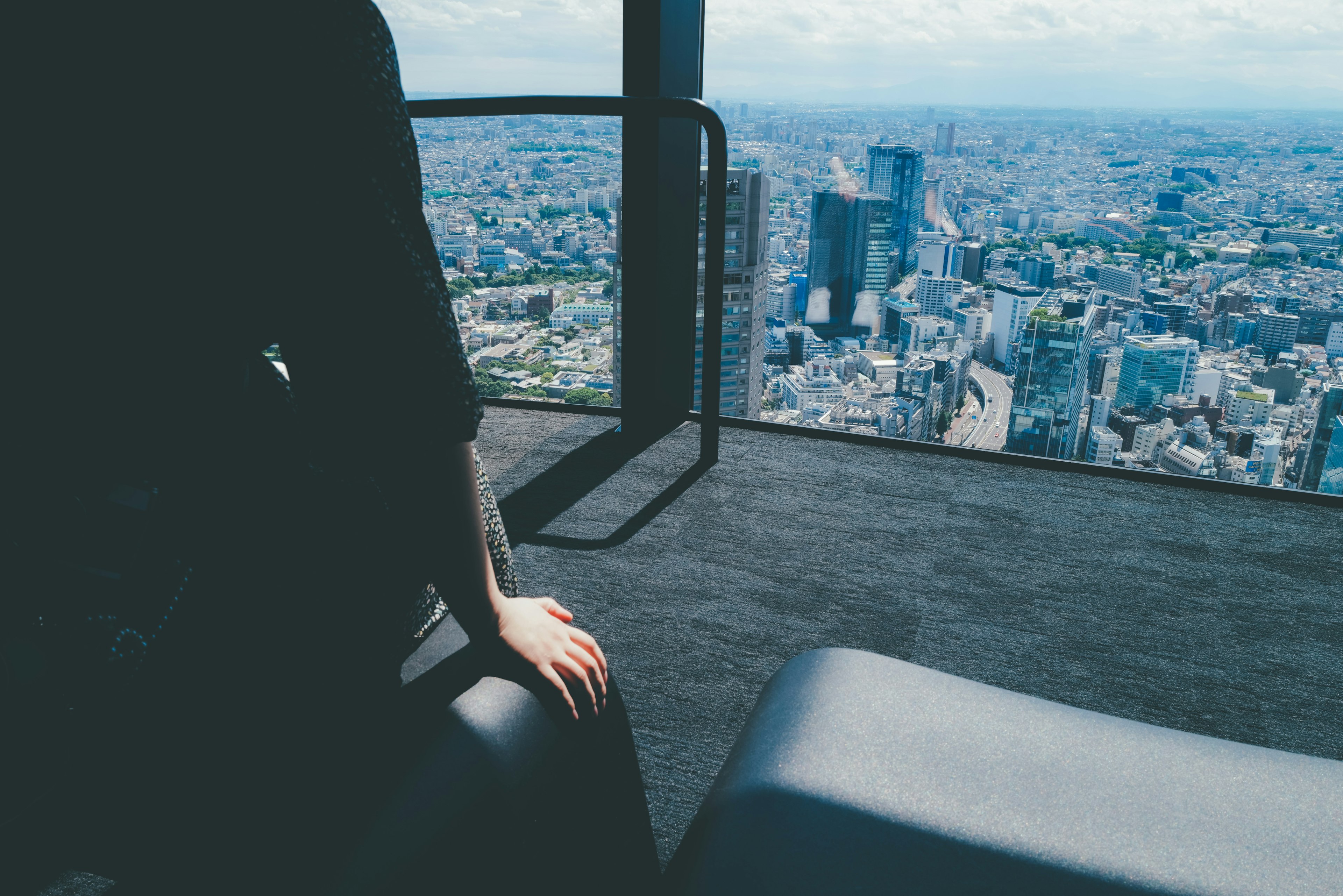 Person sitzt am Fenster mit Blick auf eine weitläufige Stadtlandschaft