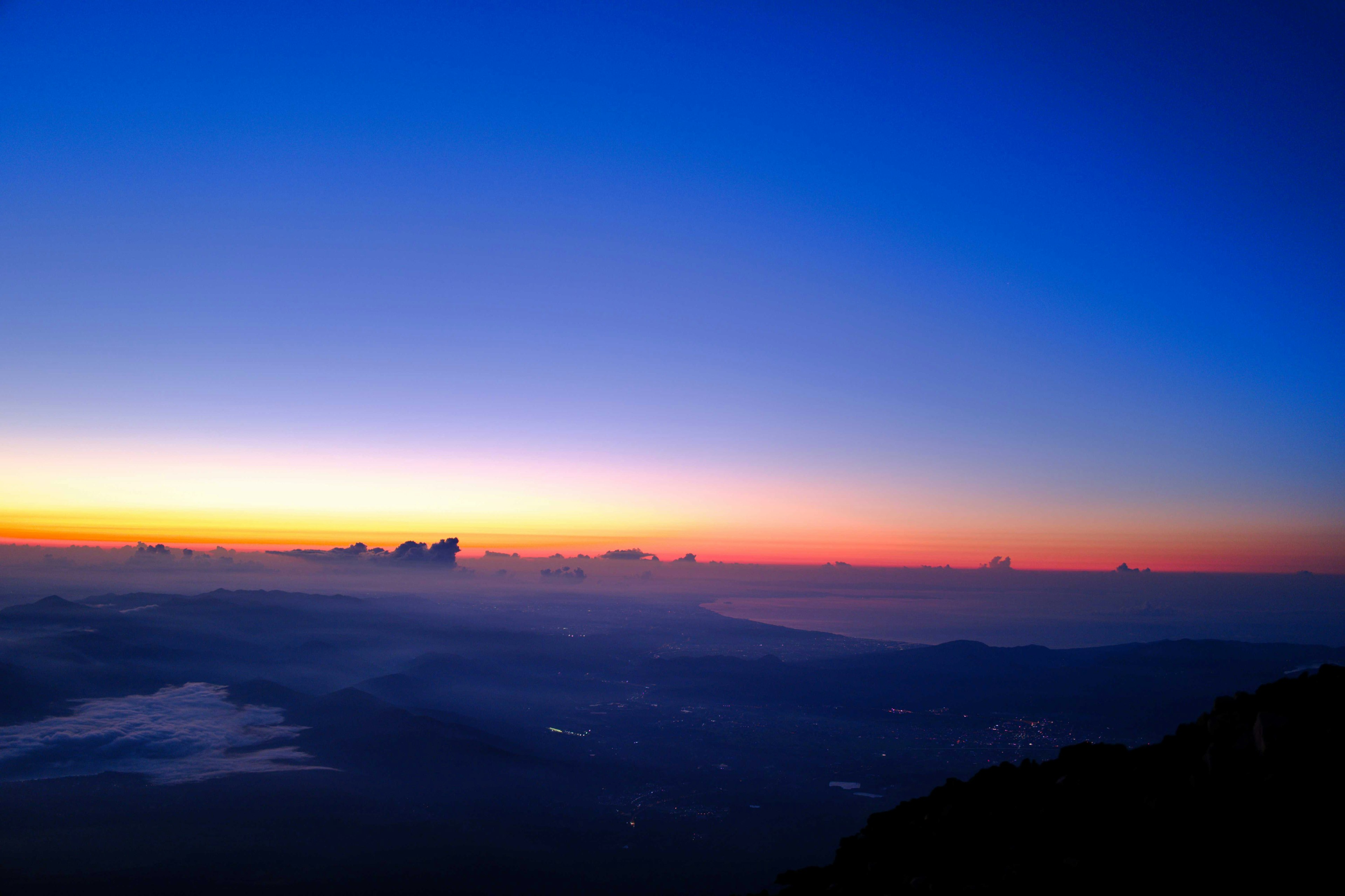 Langit fajar dengan nuansa biru dan oranye di atas lanskap pegunungan