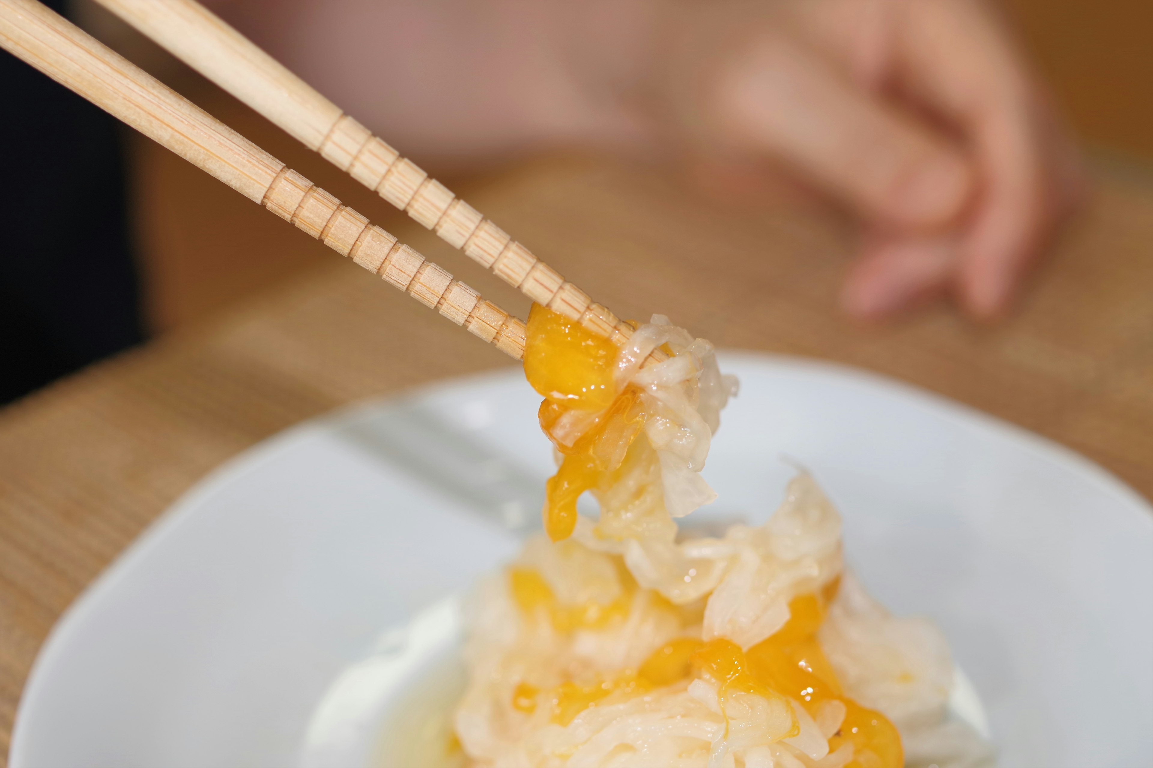 Persona usando palillos para recoger comida con yema de huevo en un plato blanco