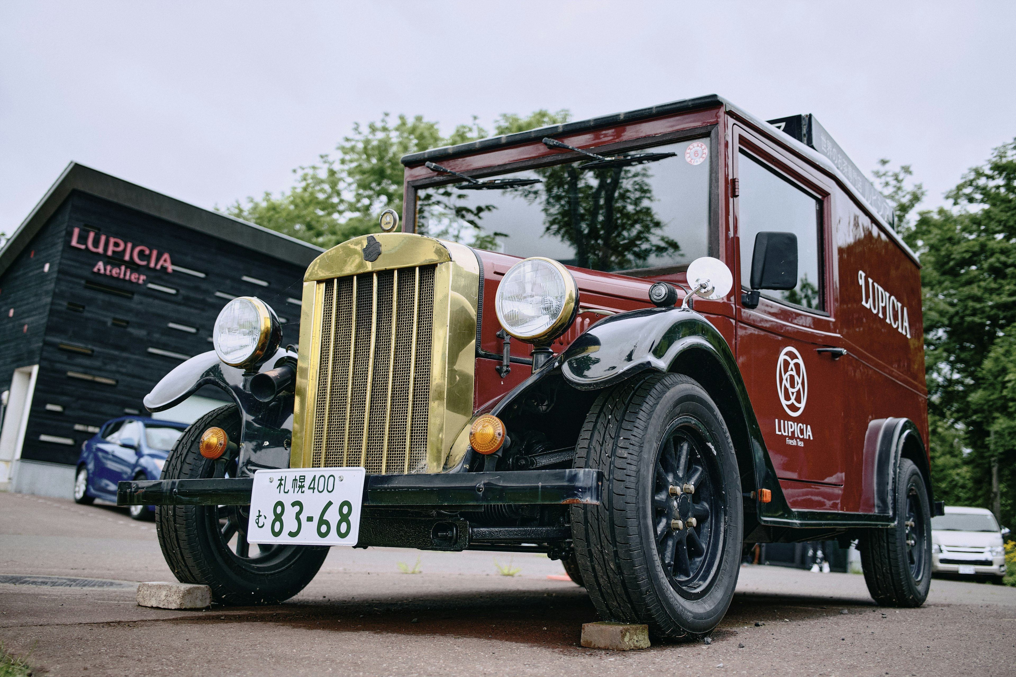 Truk merah vintage dengan gril emas dan ban putih bangunan modern di latar belakang