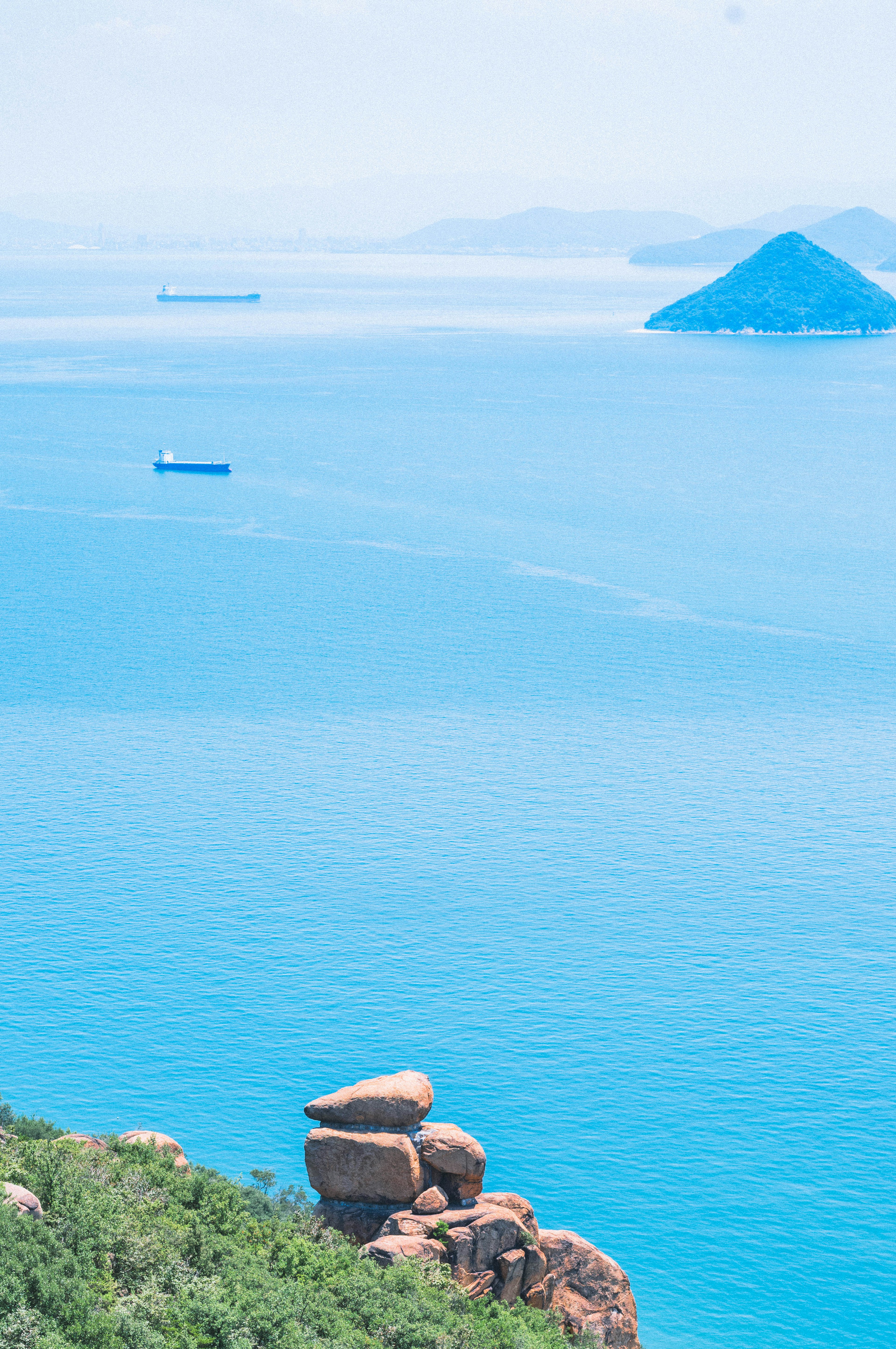 Malersicher Blick auf den blauen Ozean mit fernen Inseln und einem großen Felsen im Vordergrund