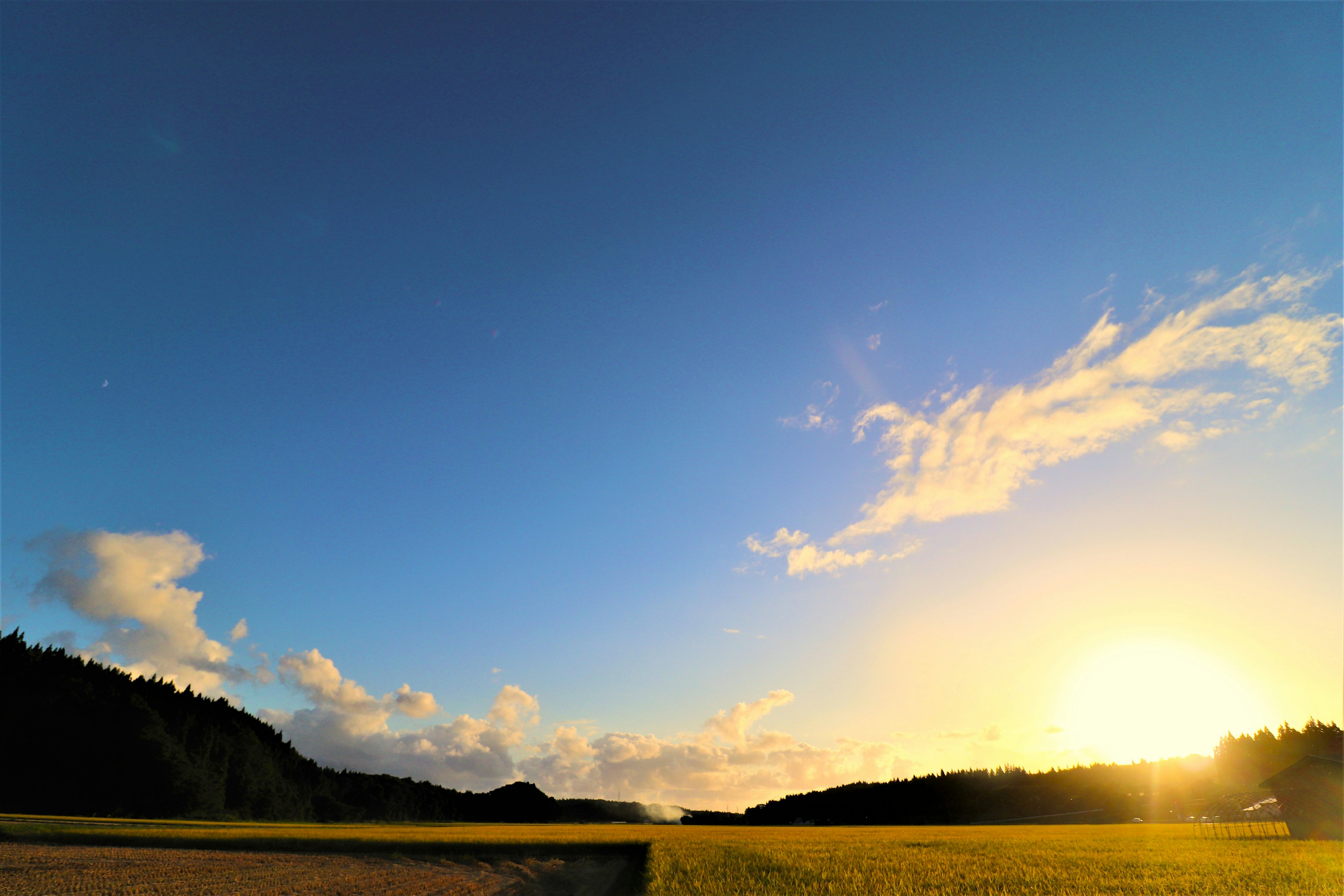 青空と雲が広がる夕暮れの風景 太陽が沈みかける田園風景