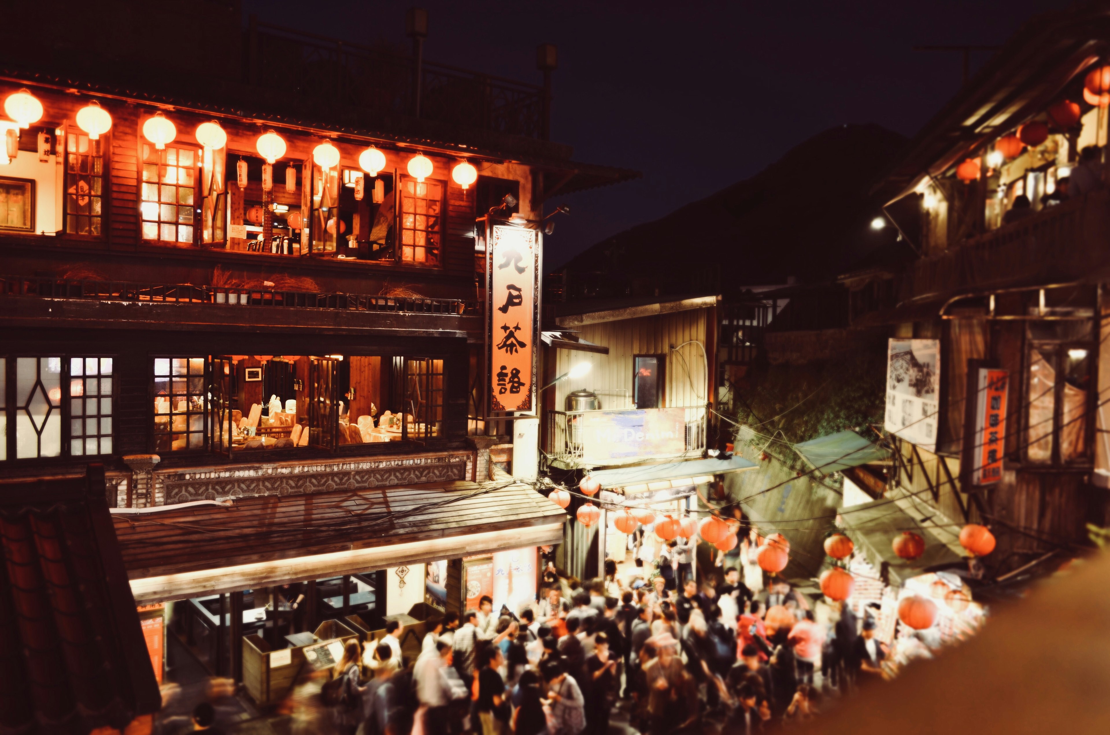 Night scene of a bustling street with red lanterns and crowds of people