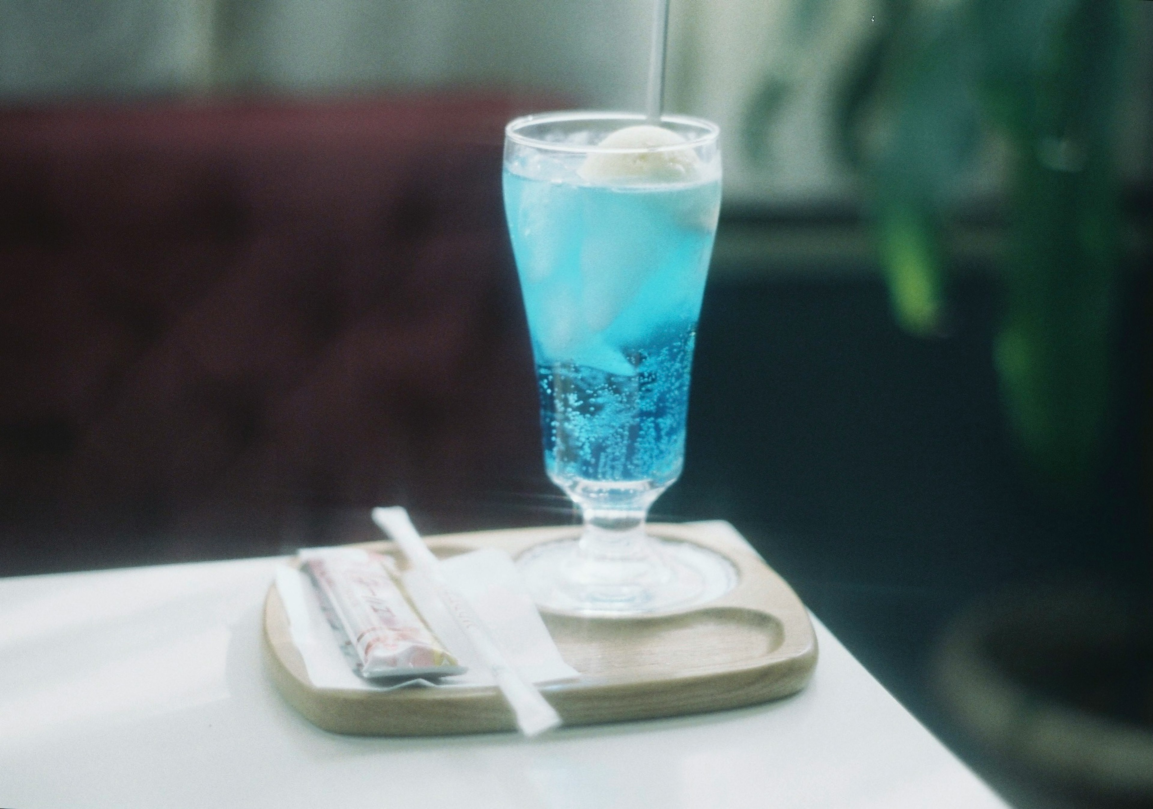 A glass of blue drink with ice cream on top placed on a wooden tray