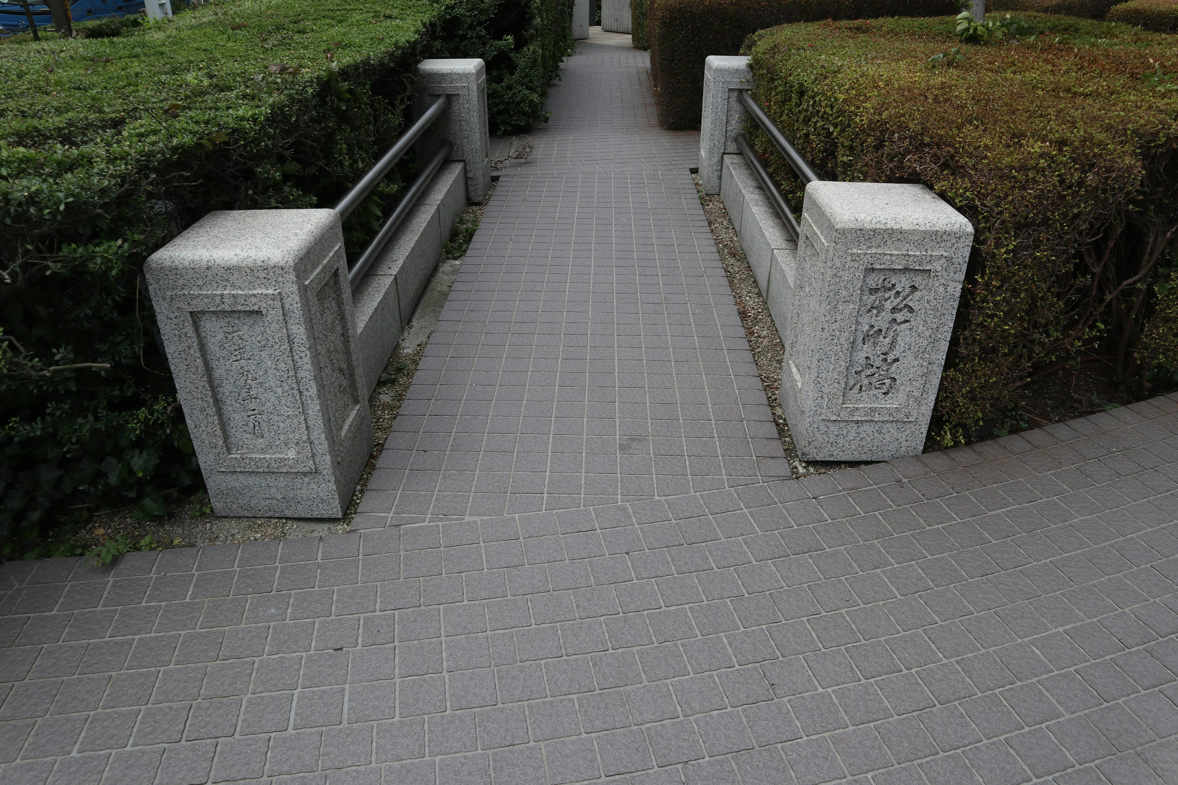 Paved walkway with concrete barriers and low hedges