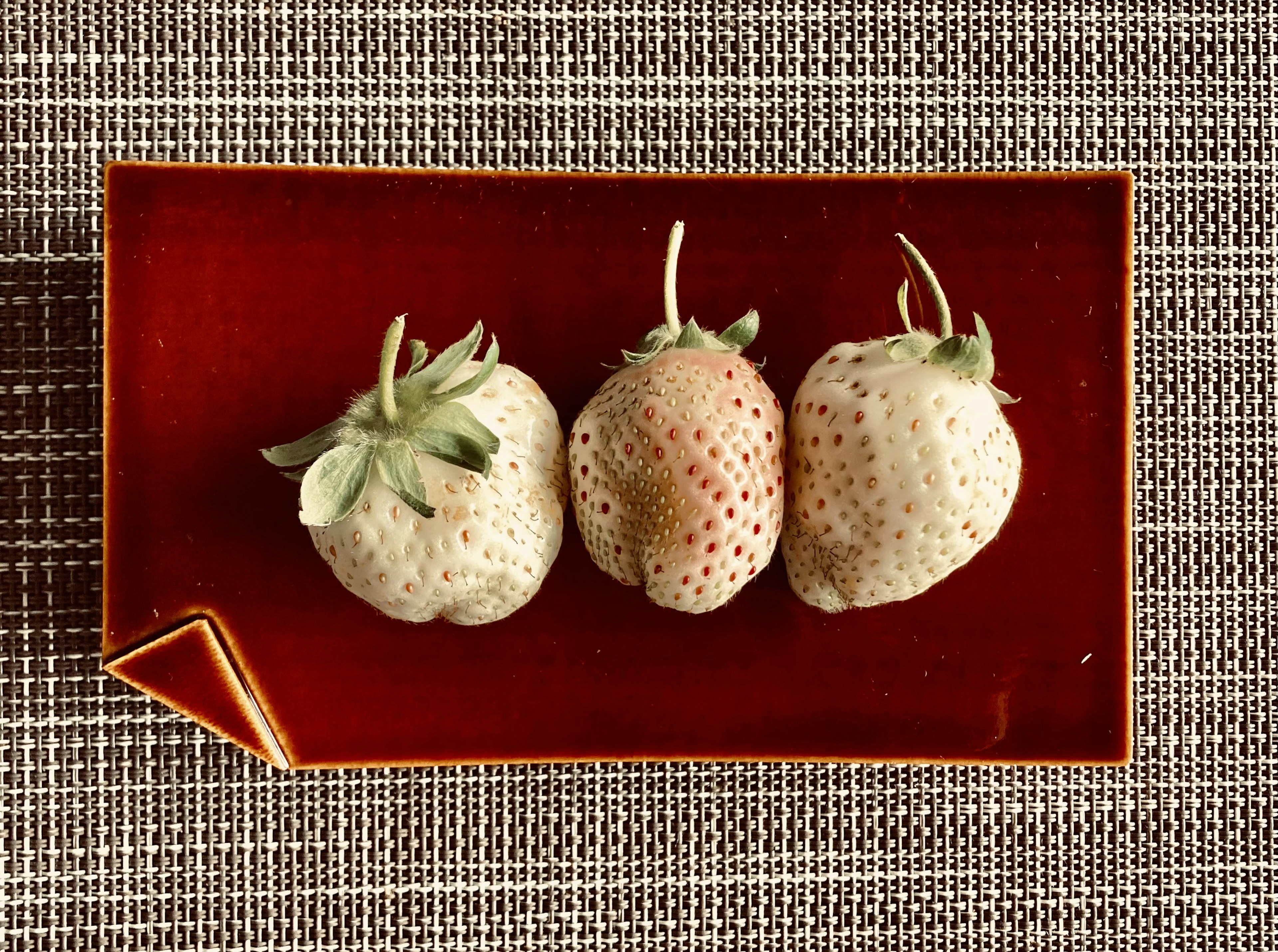 Three pale strawberries arranged on a red plate