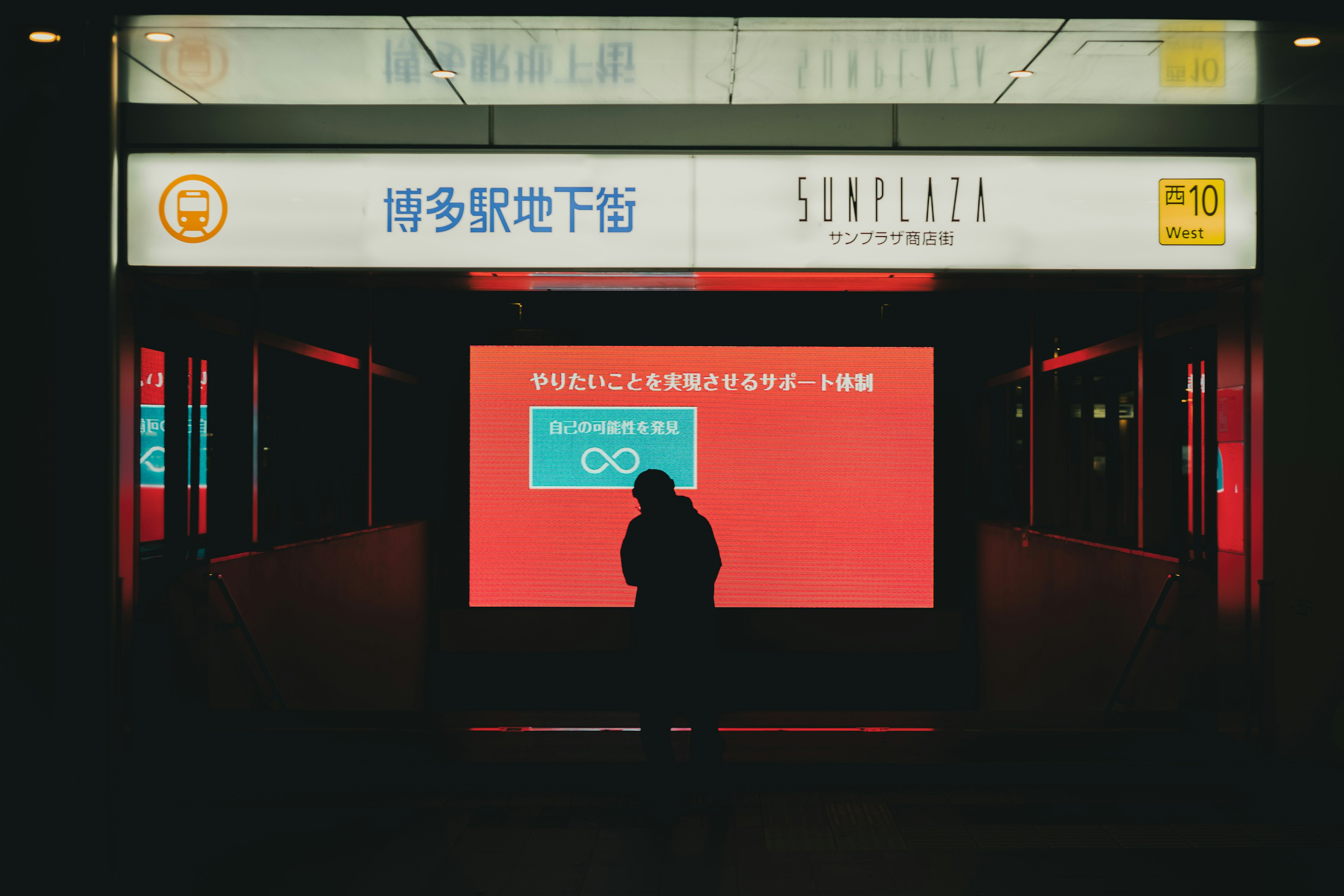 Silhouette standing in front of a red background and subway station sign