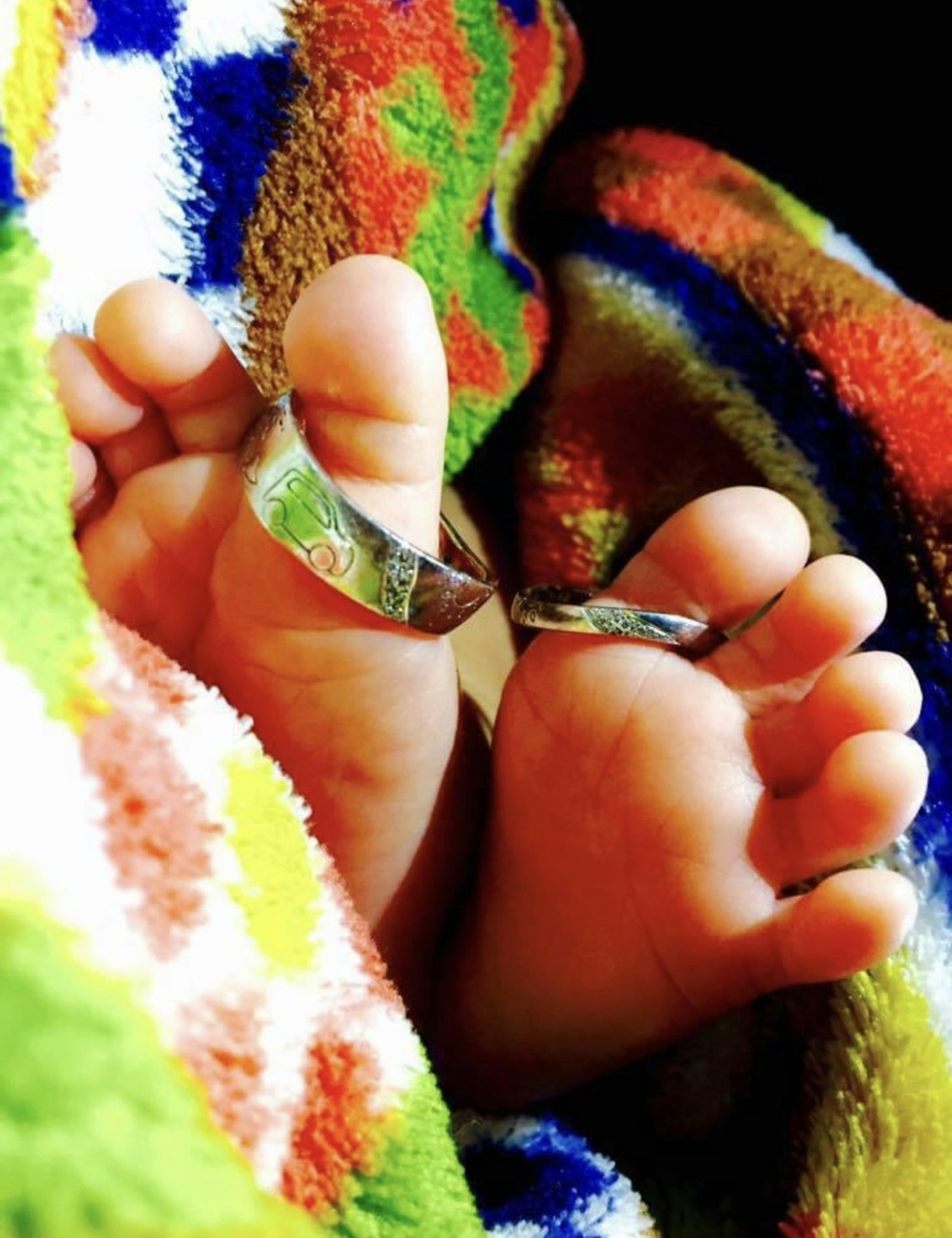 Baby feet wrapped in a colorful blanket with a ring