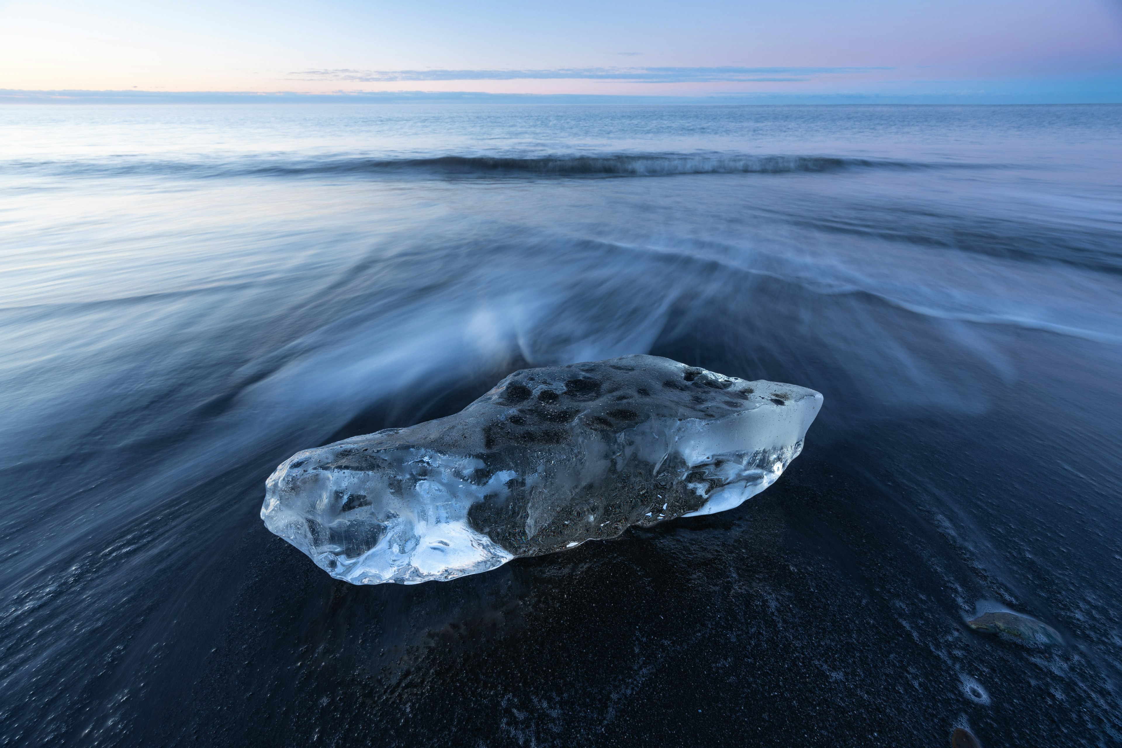 Un morceau de glace reposant sur une plage de sable noir avec des vagues douces