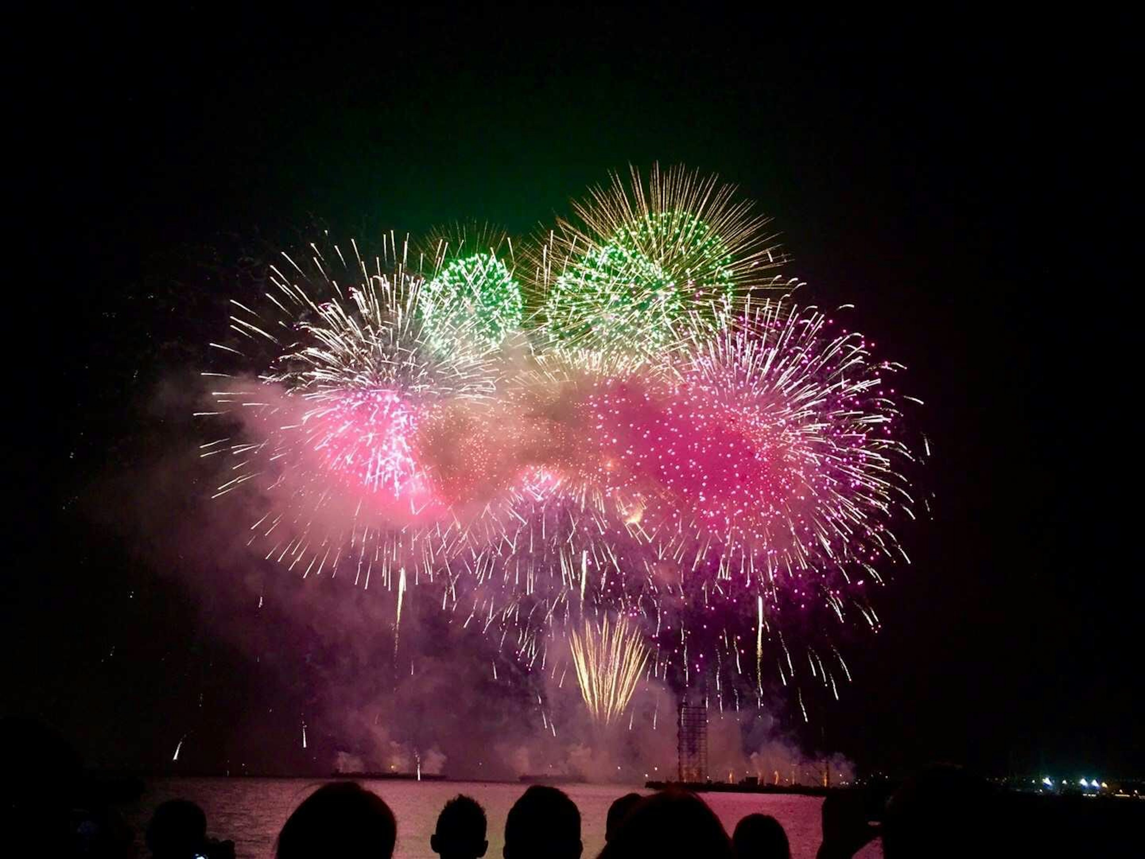 夜空に輝くカラフルな花火のショー観客のシルエットが見える