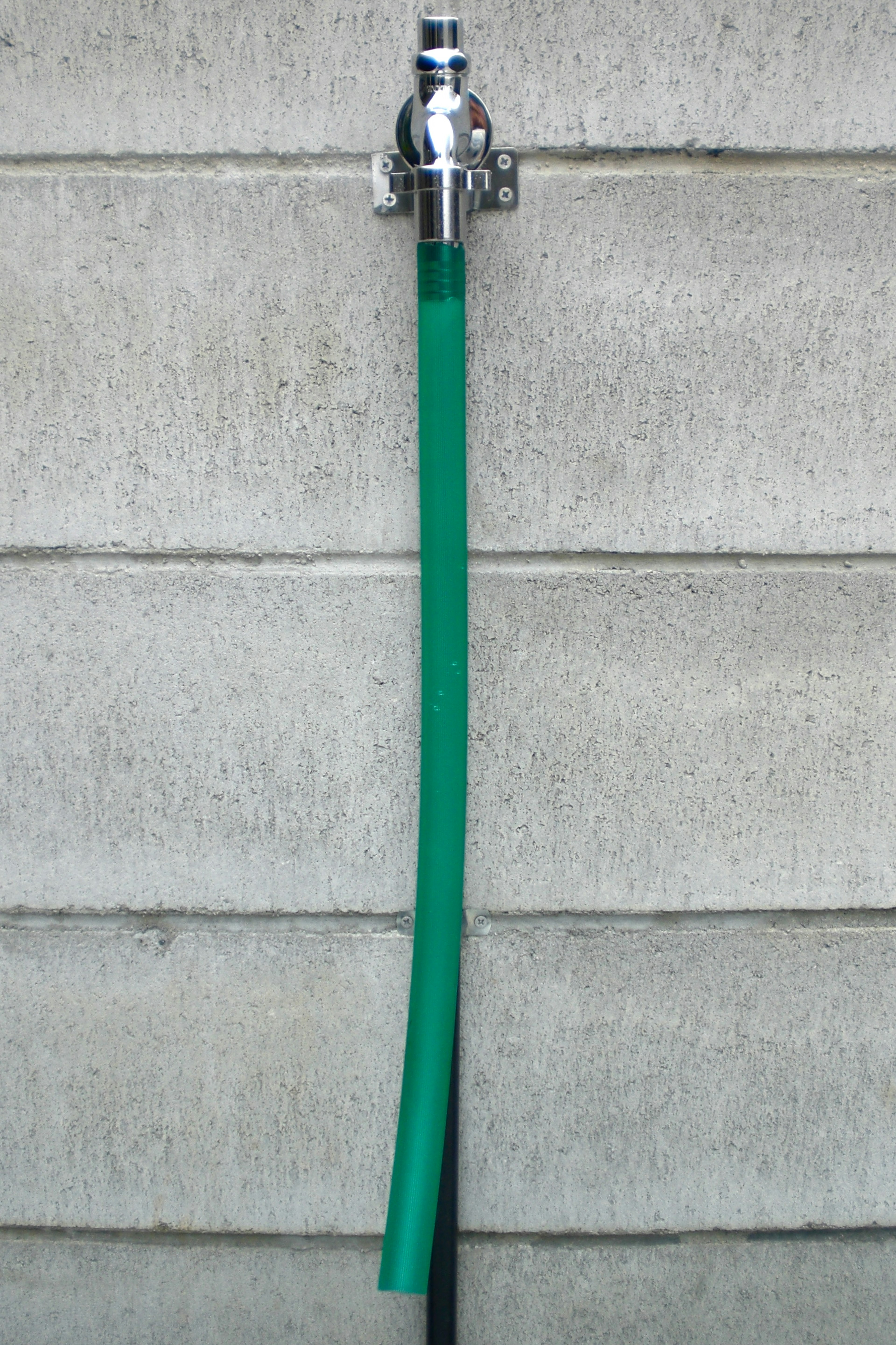 Green hose attached to a faucet on a concrete wall