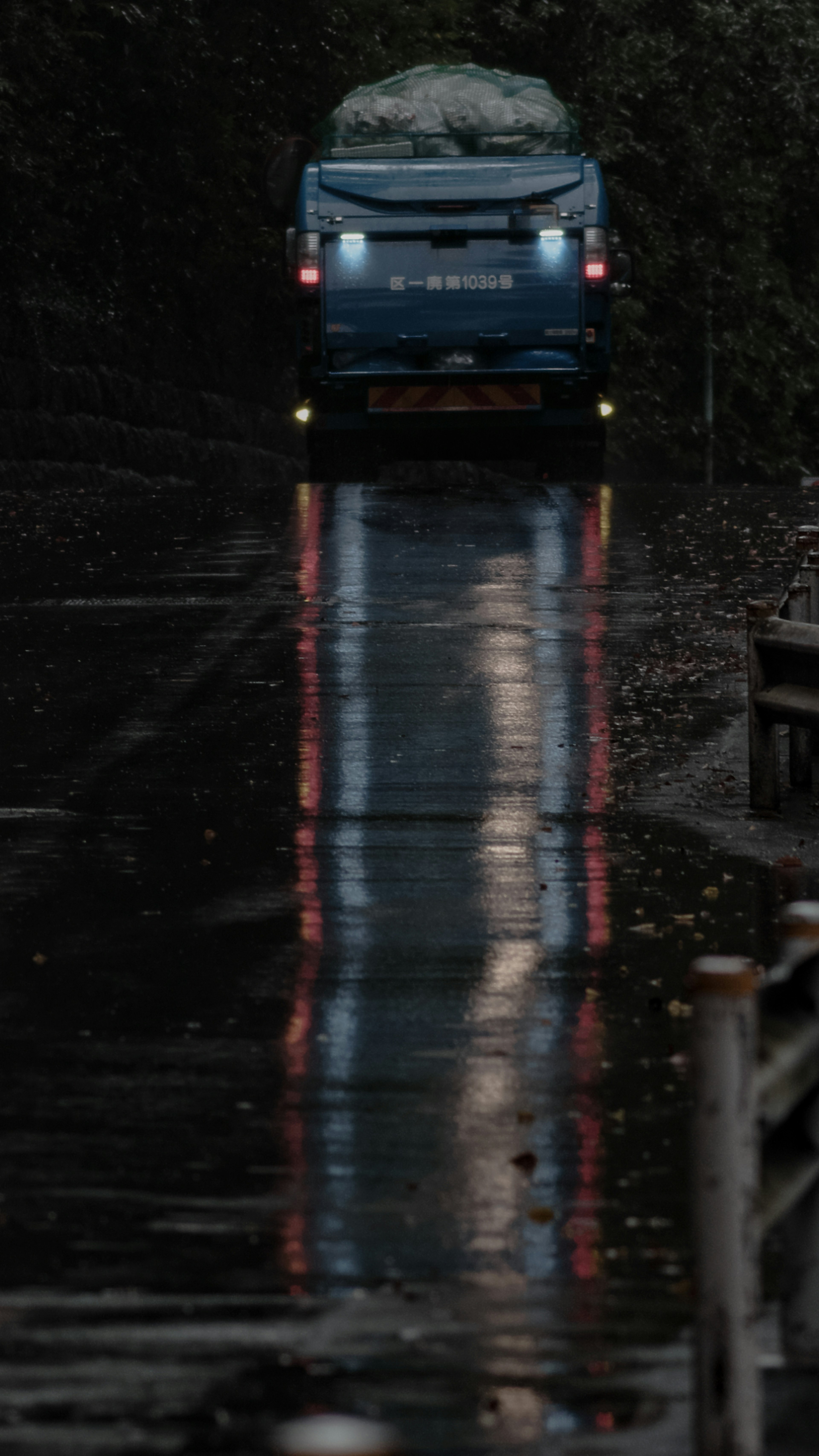 Un veicolo blu che percorre una strada bagnata con riflessi