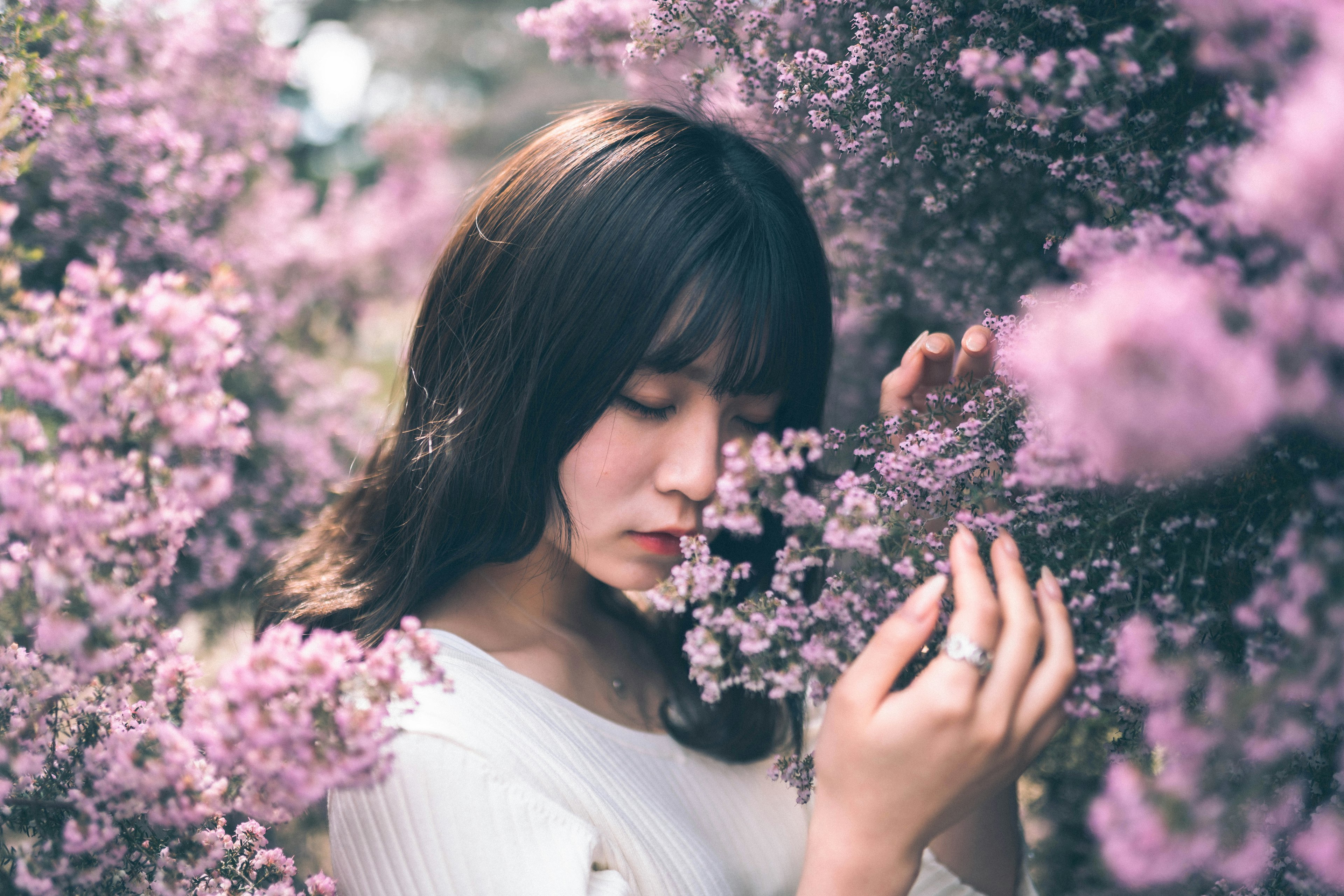 Seorang wanita dikelilingi bunga ungu dengan lembut menikmati aromanya