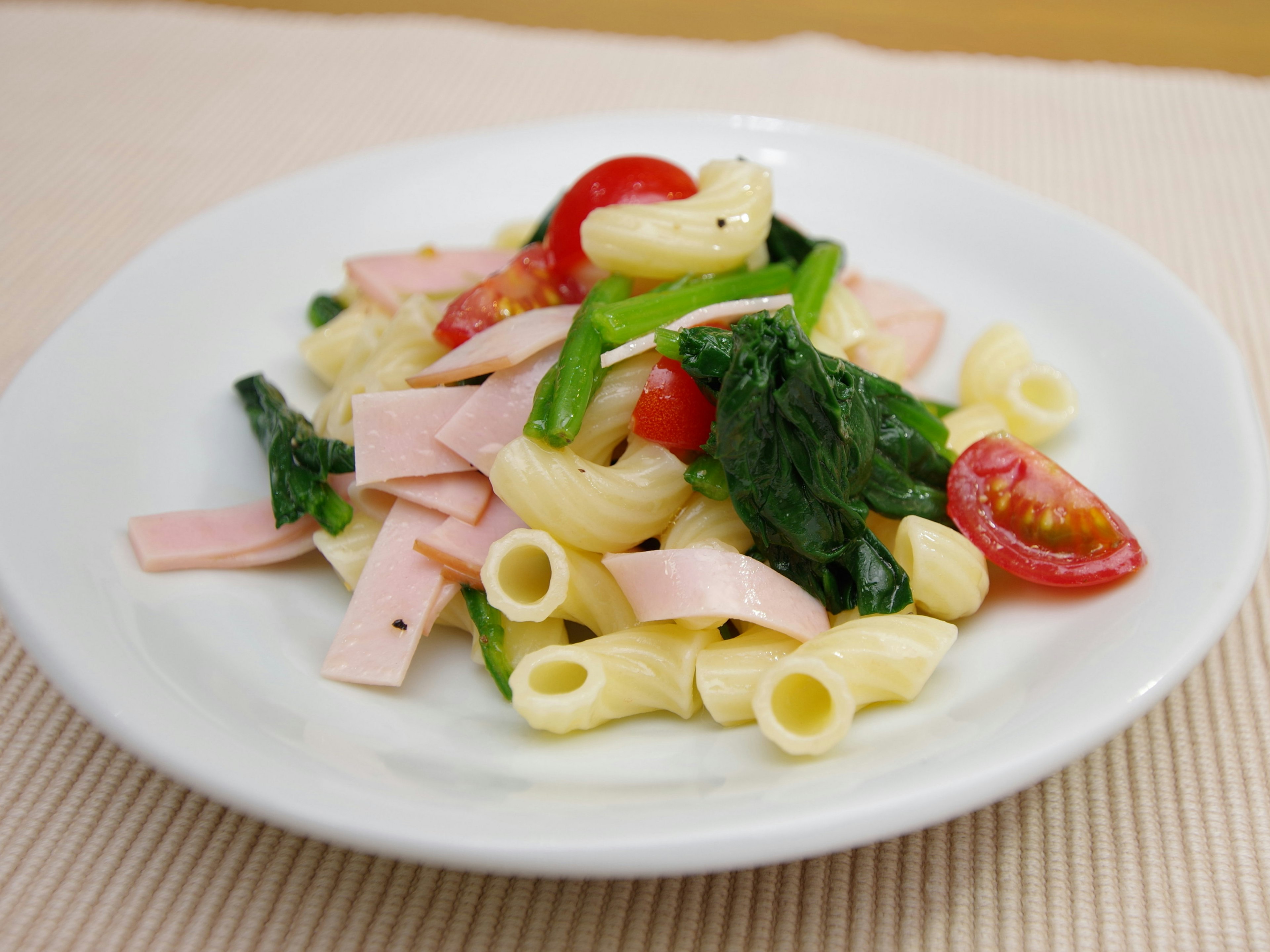 Pasta salad with ham, tomatoes, and spinach on a white plate