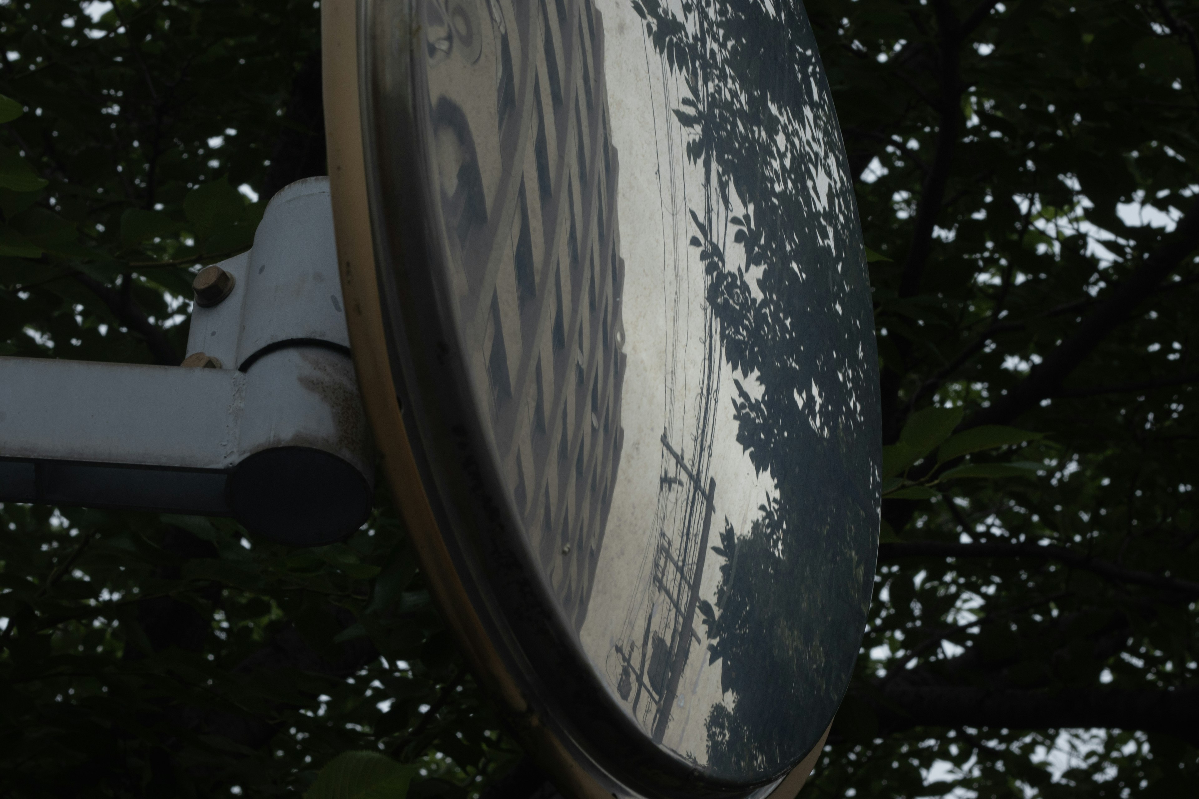 Image of a reflective mirror featuring trees and a building in its reflection