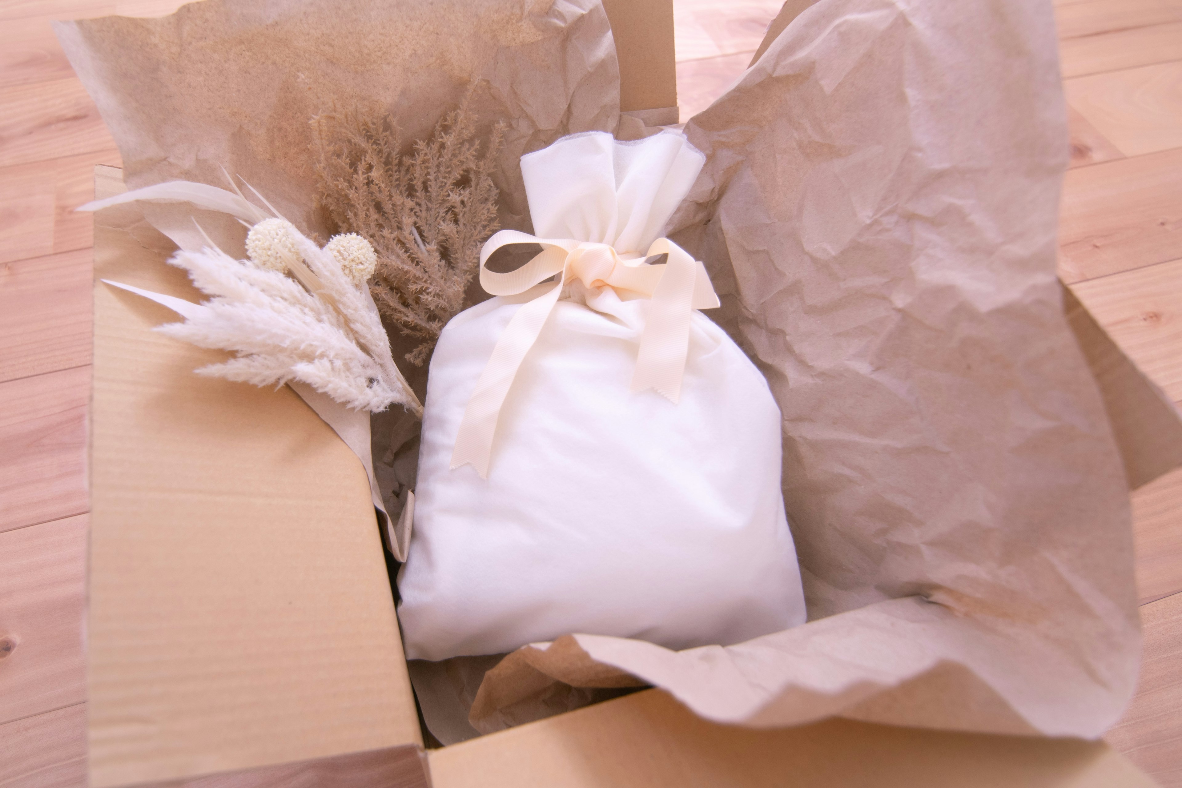 A cardboard box containing a small white fabric pouch and dried plants