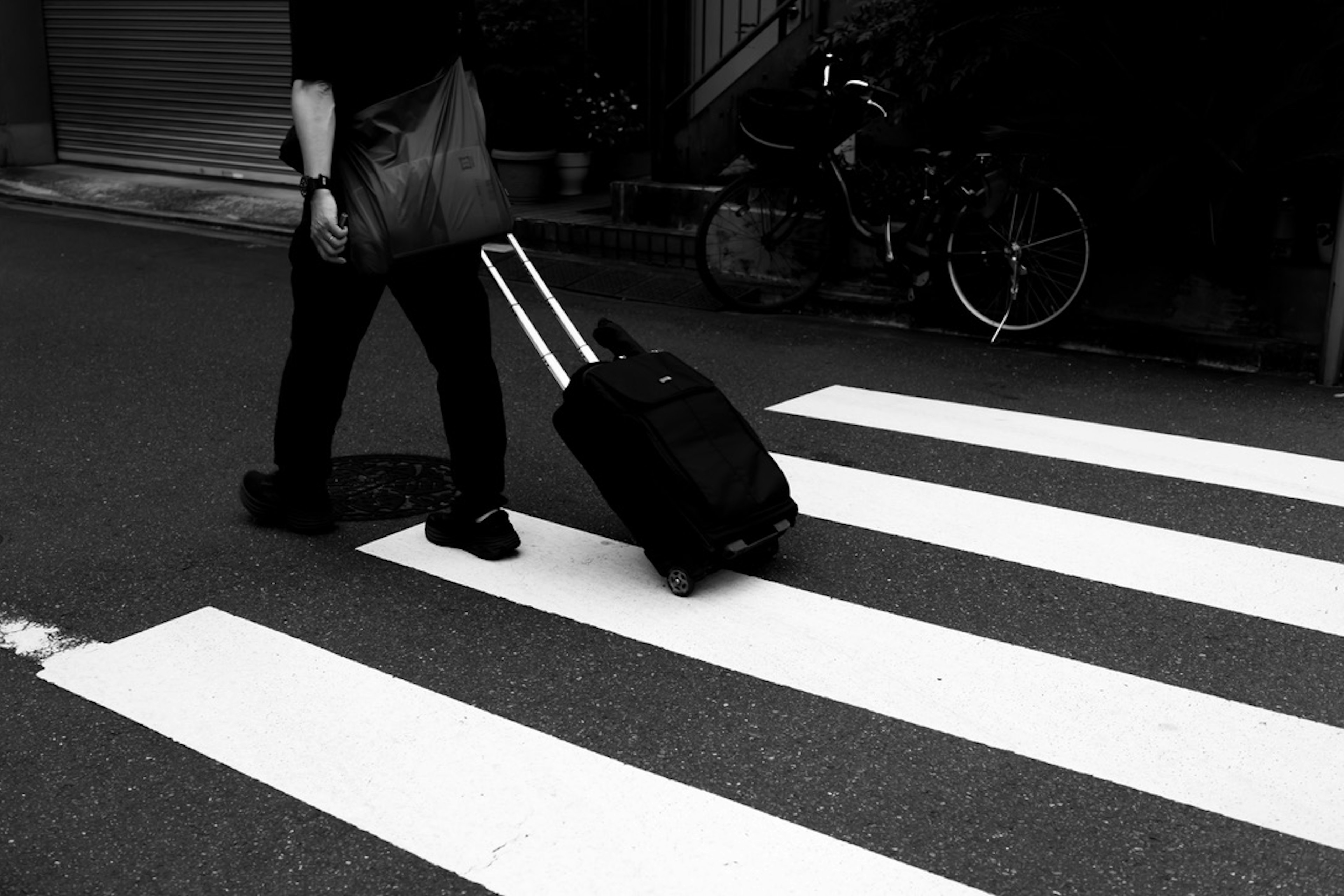 白い横断歩道を渡る旅行者と黒いスーツケース