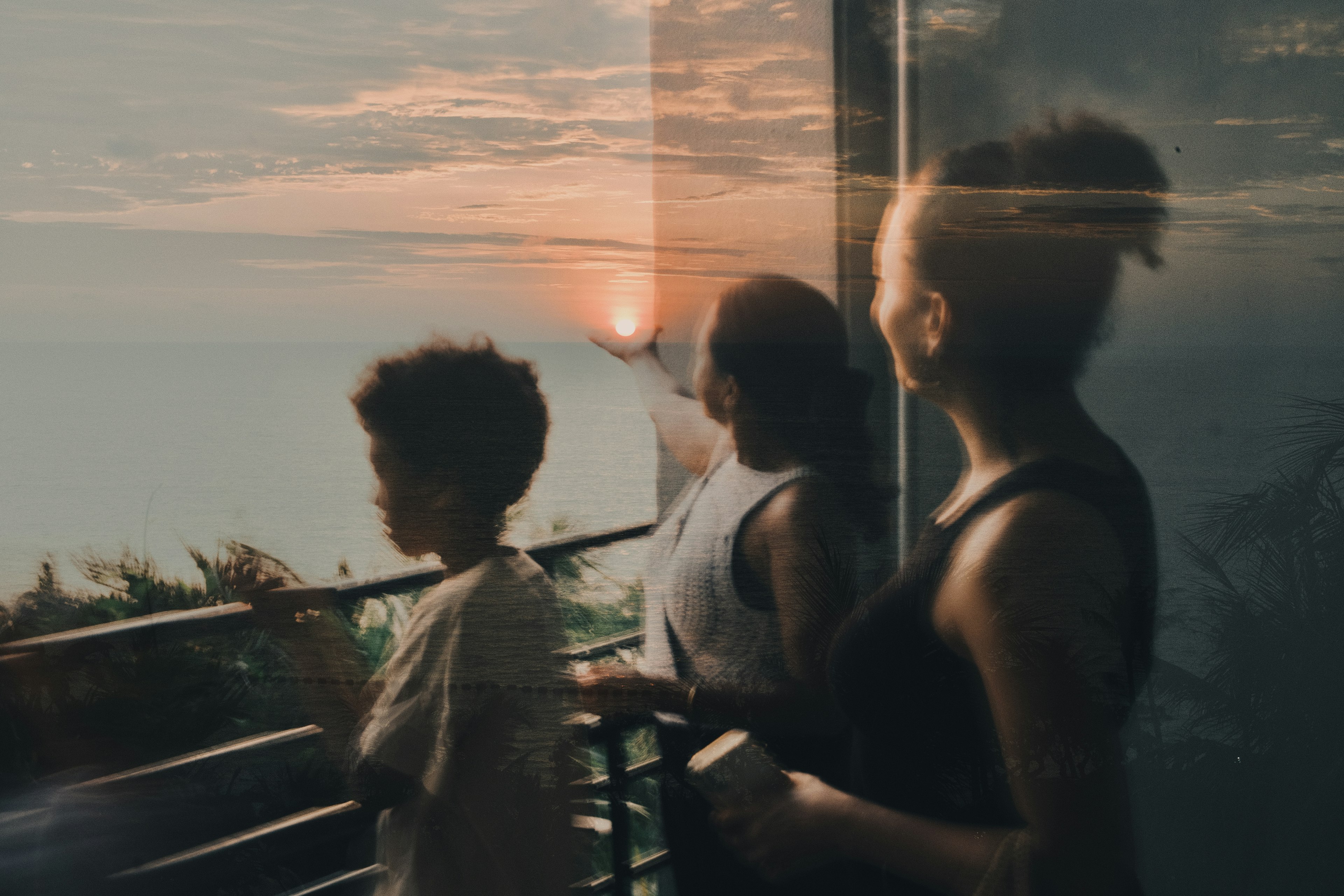 夕日を眺める3人のシルエットと海の景色