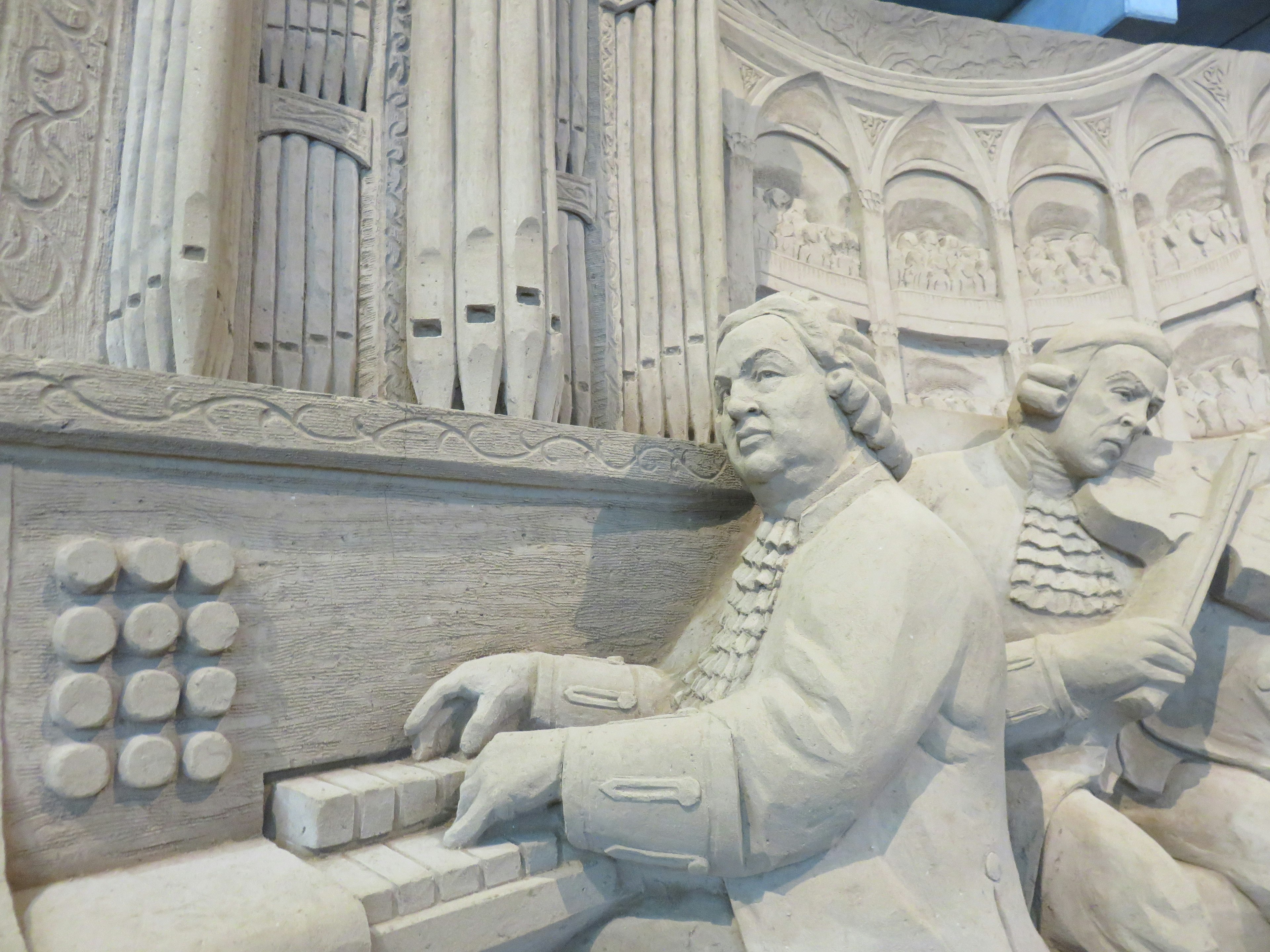 Detailed sculpture of two musicians playing an organ resembling Bach