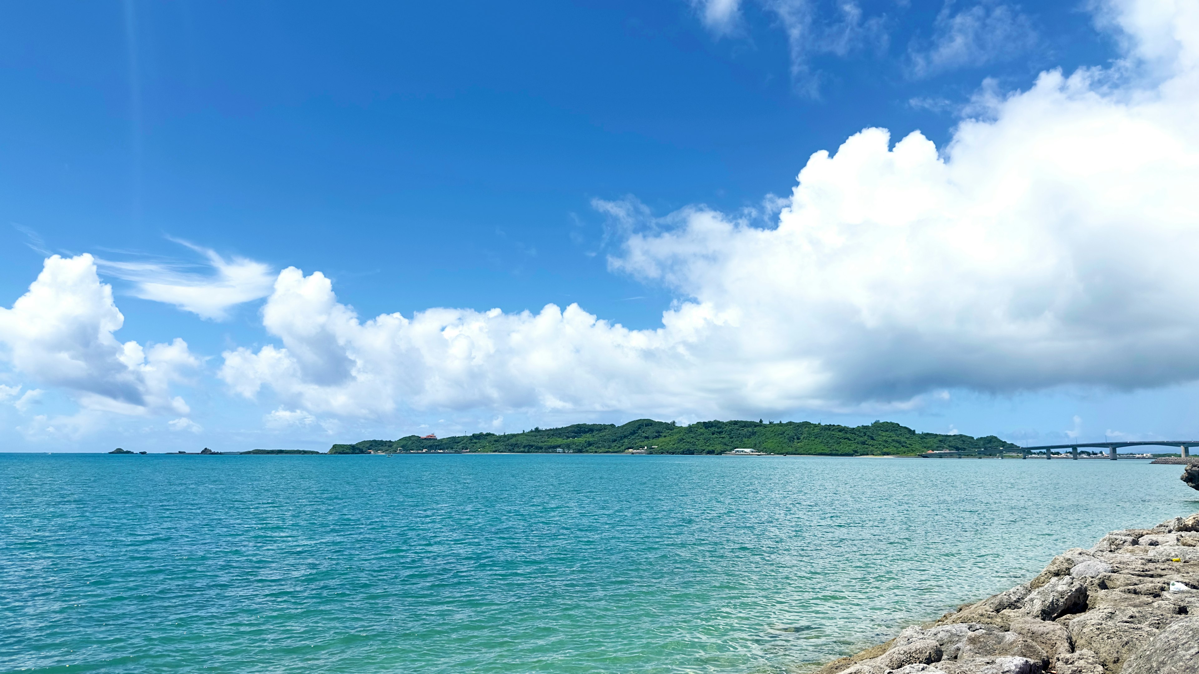 Panoramic view of blue ocean with white clouds green island in the background