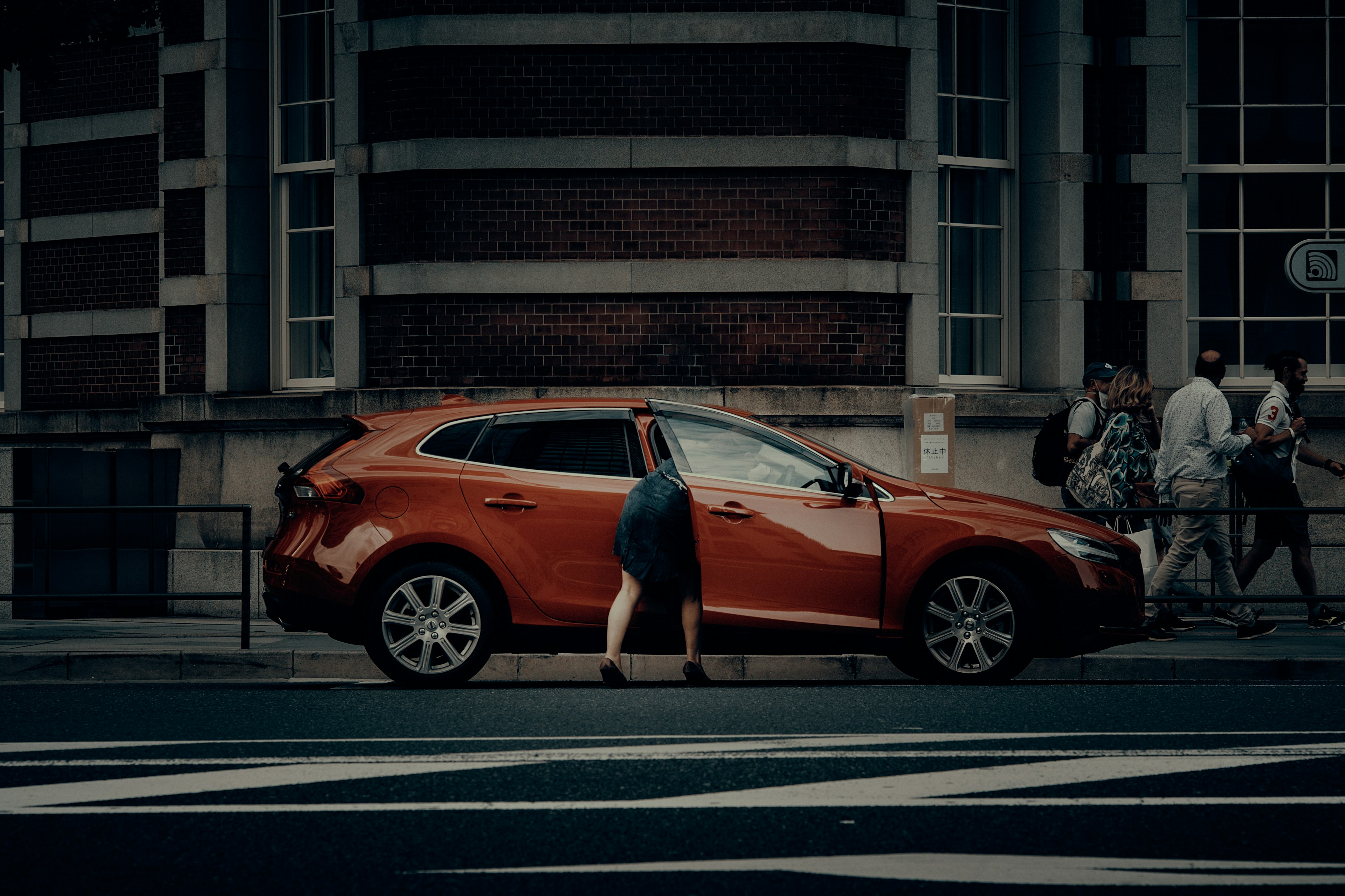 A person searching for something near a red car in an urban setting