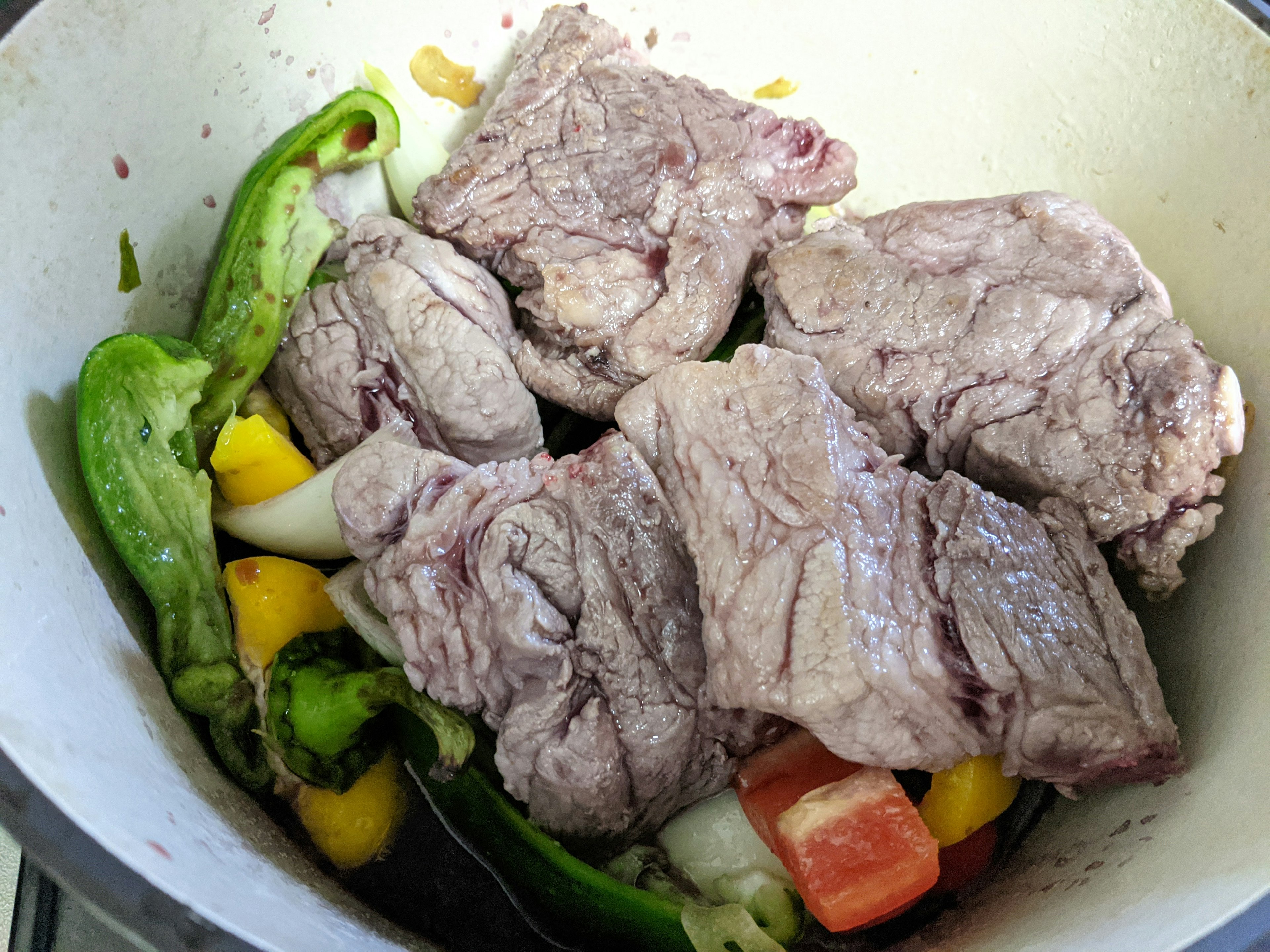 Chunks of meat placed in a pot with green and yellow vegetables