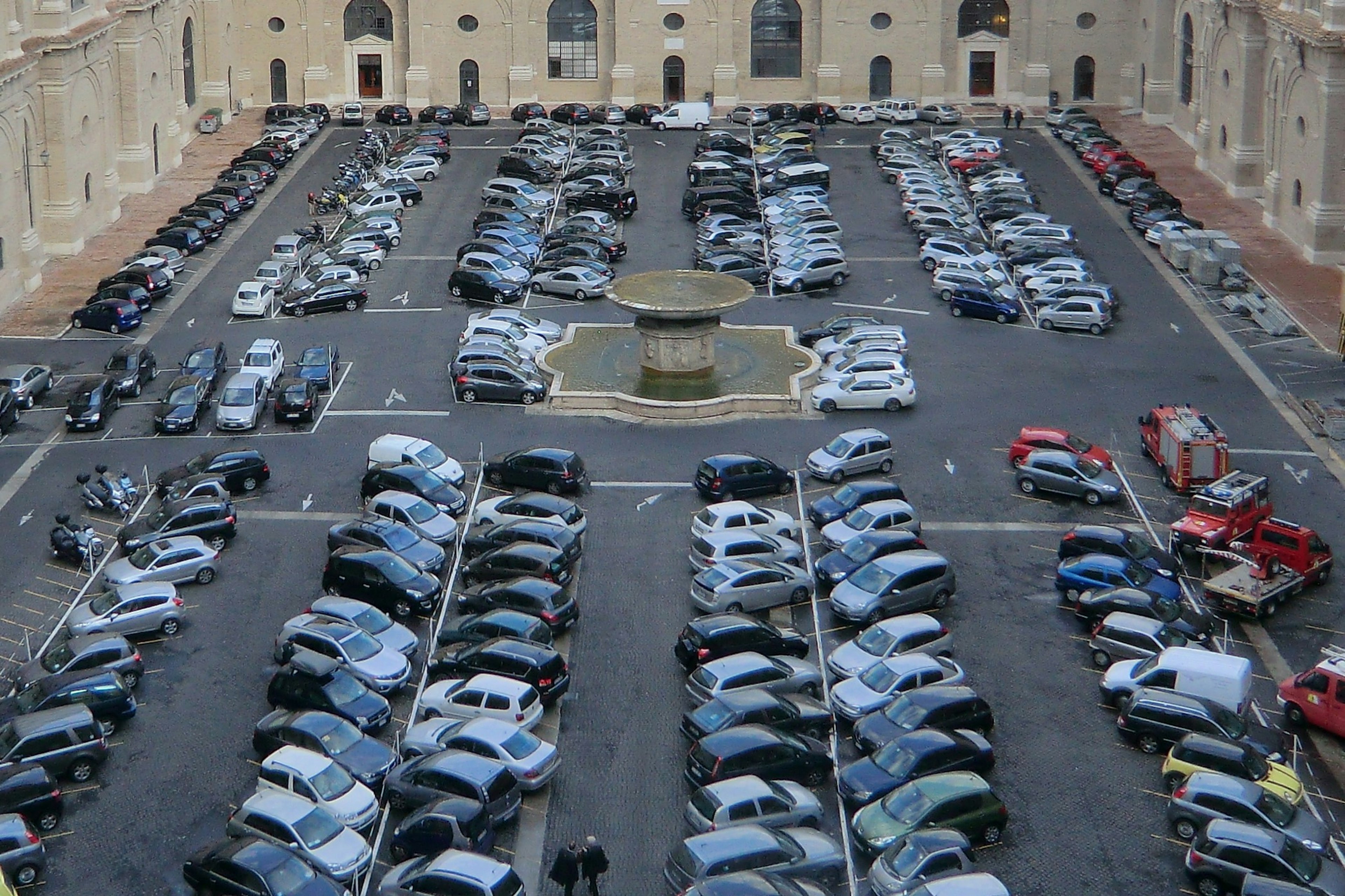 Un grande parcheggio pieno di auto diverse e una fontana centrale