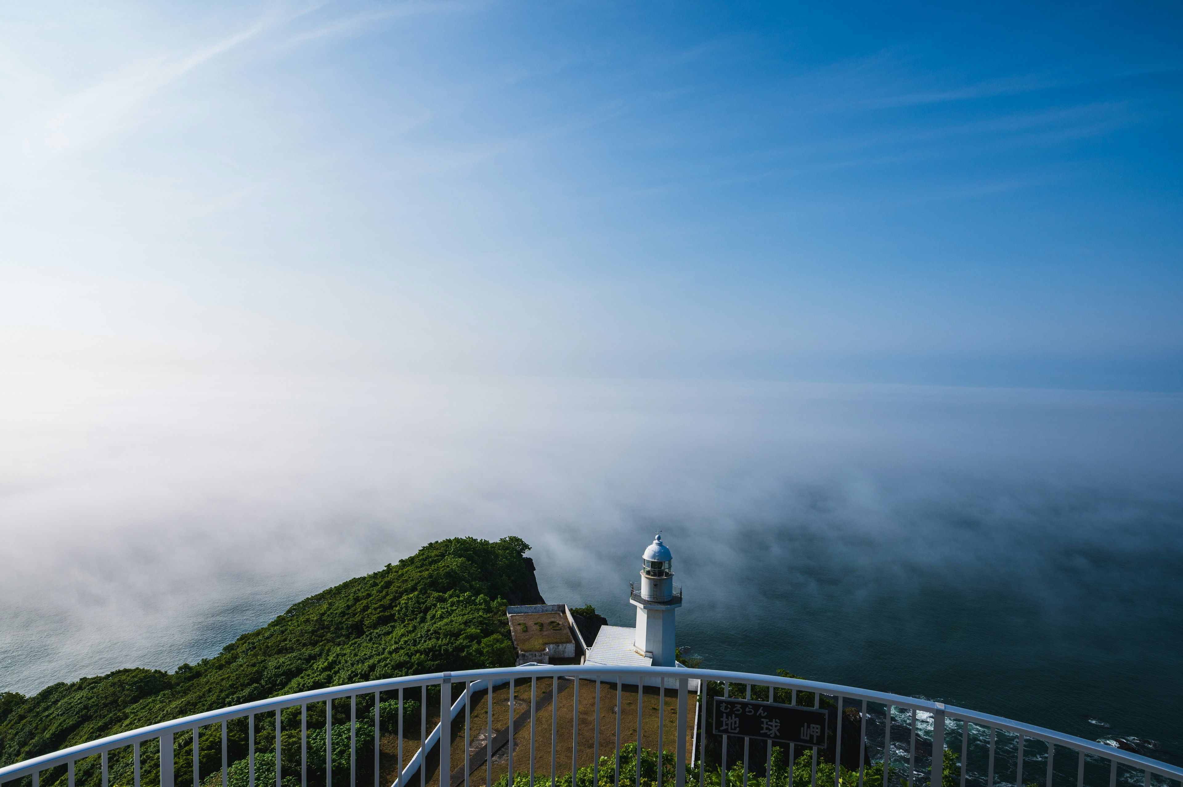 Vista panoramica di un faro su una costa nebbiosa sotto un cielo blu