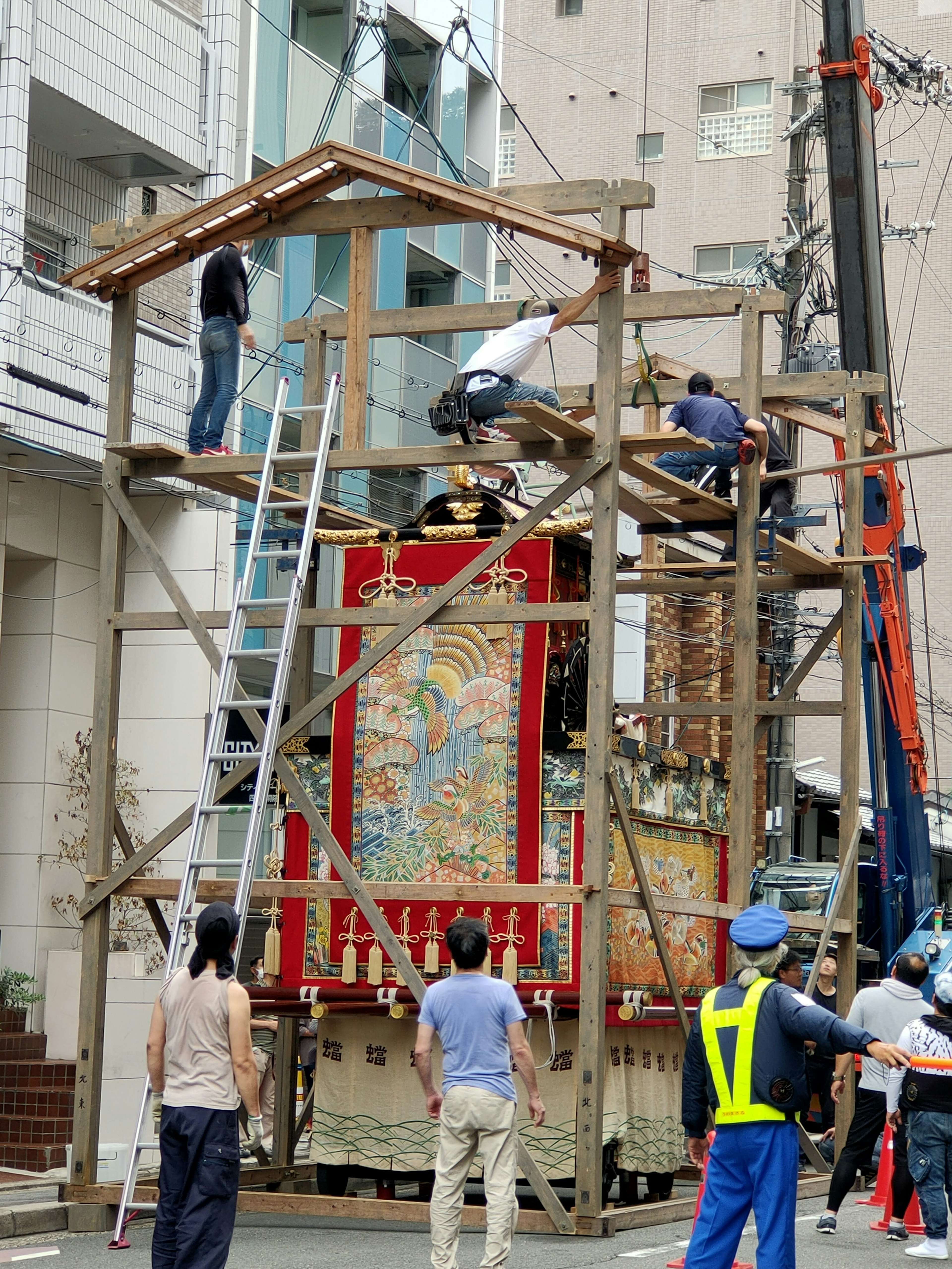 축제를 위한 차량을 조립하는 작업자들과 배경의 구경꾼들