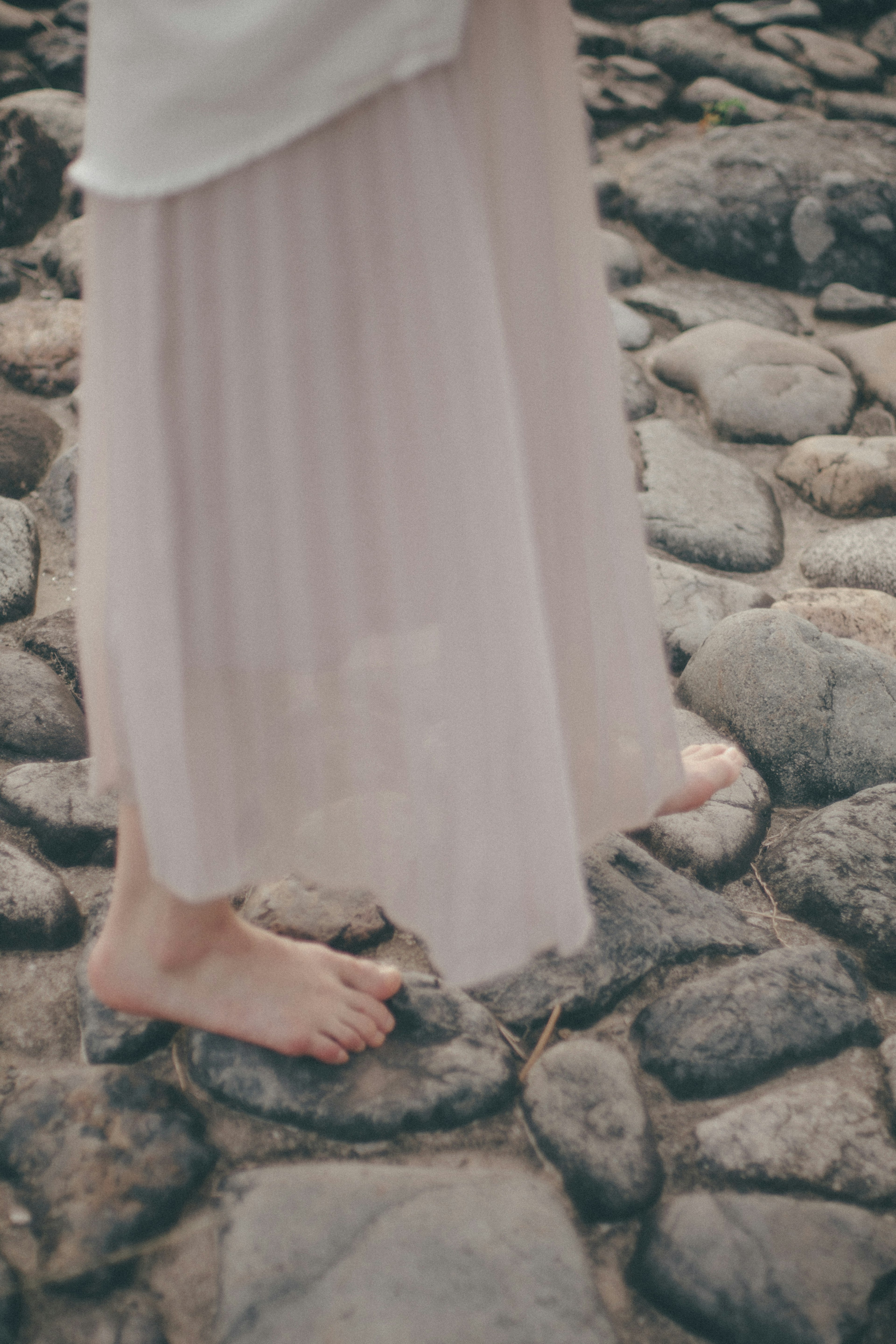 A woman's bare feet on stones while wearing a flowing light skirt