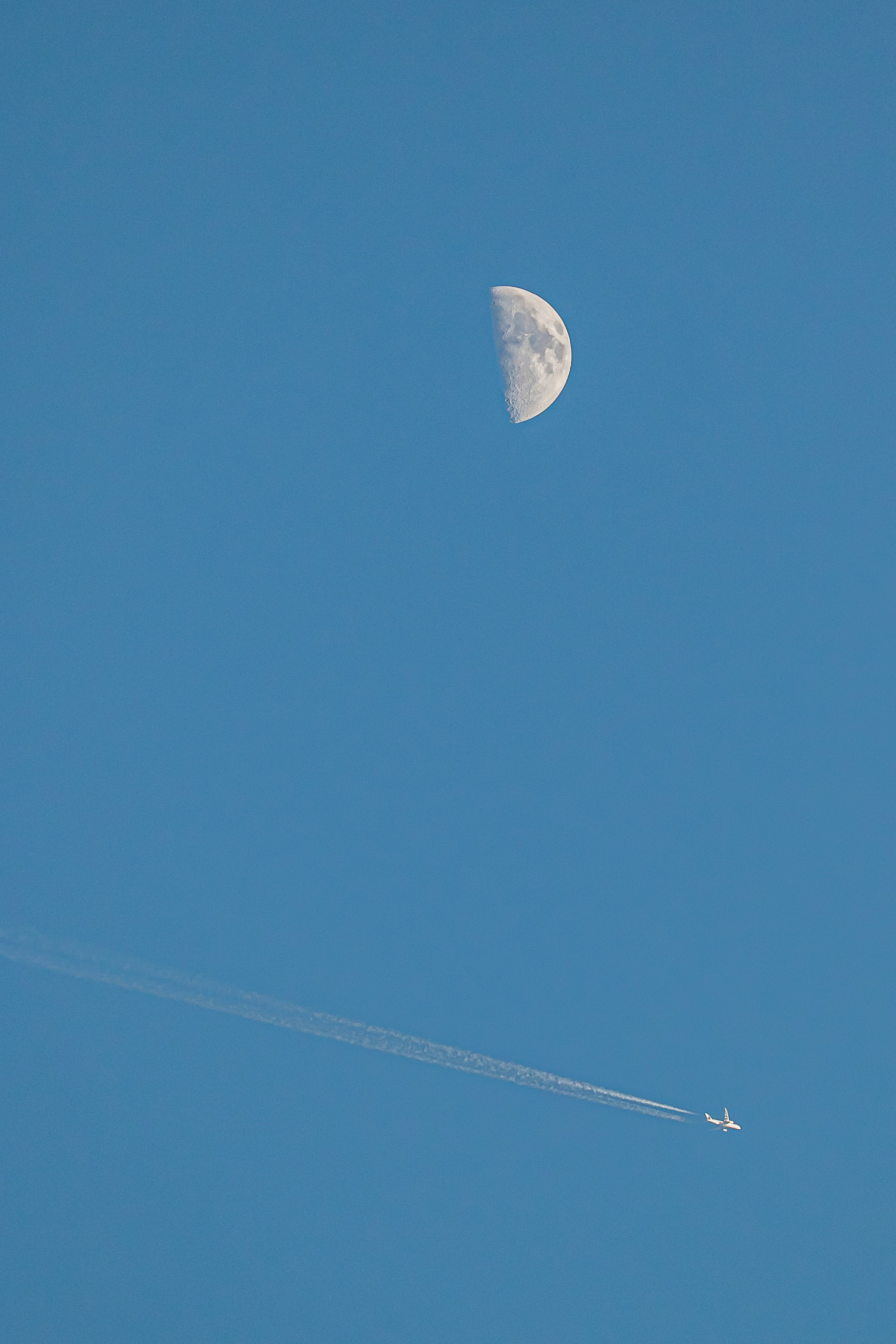 Moon in the blue sky with an airplane contrail