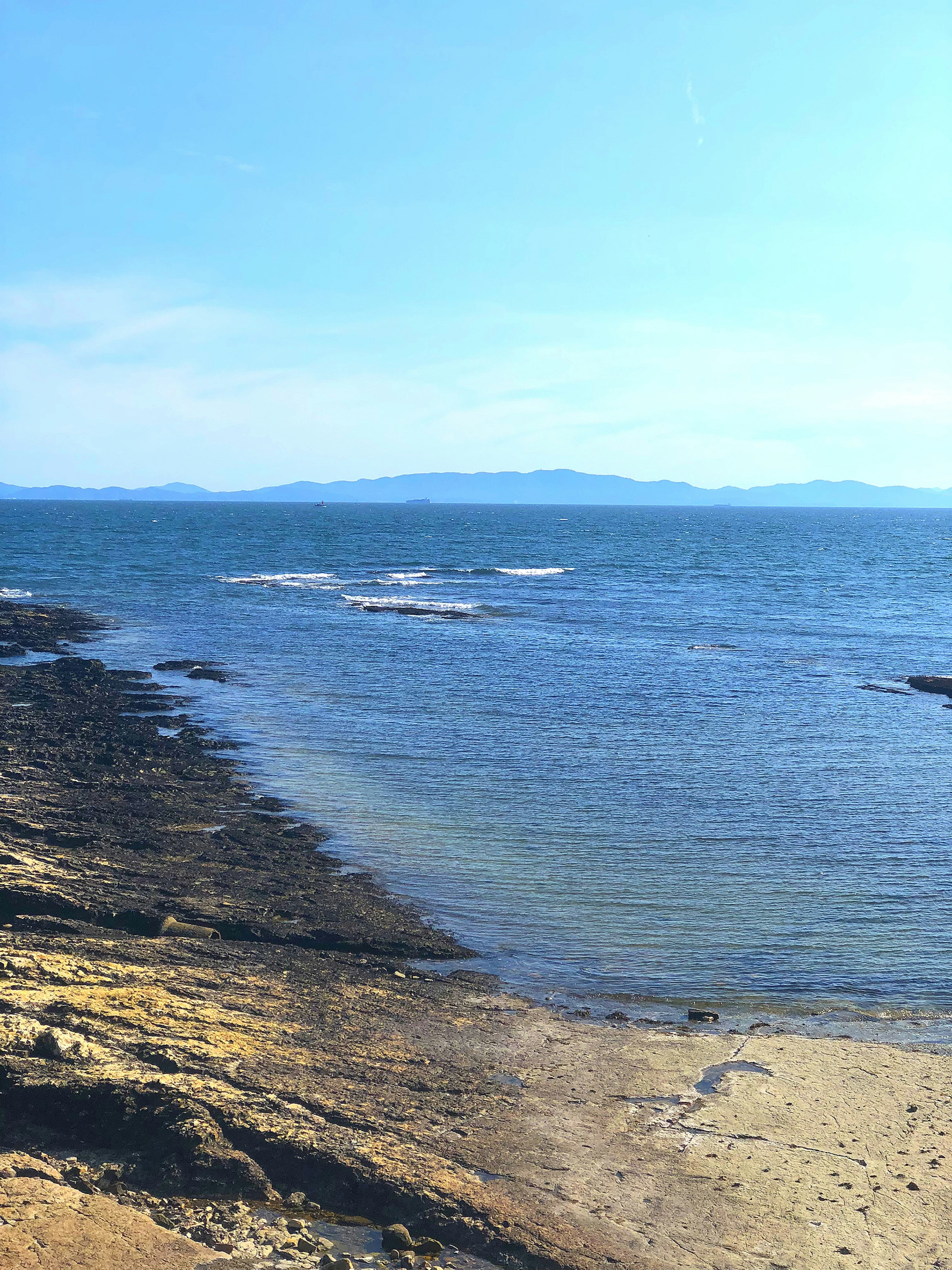 Pemandangan laut tenang dan langit biru dengan pantai berbatu dan berpasir