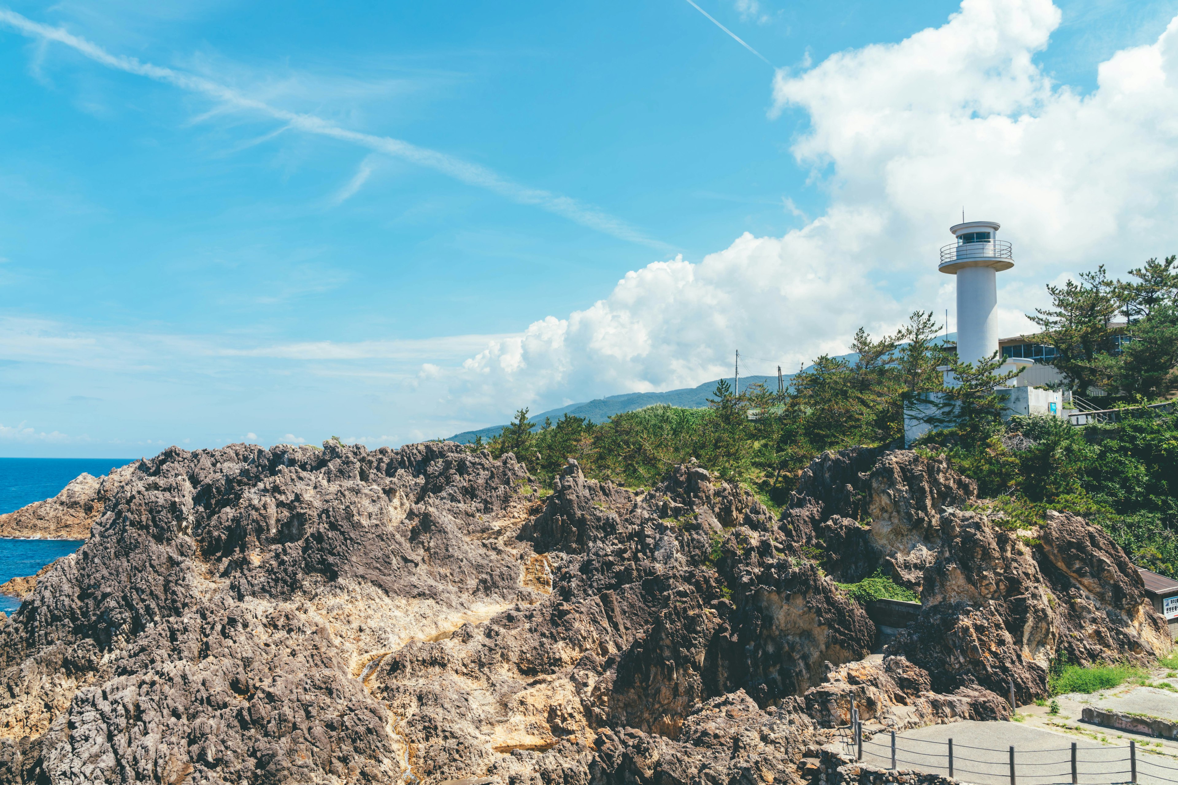 Vista panoramica della costa rocciosa con un faro sotto un cielo blu