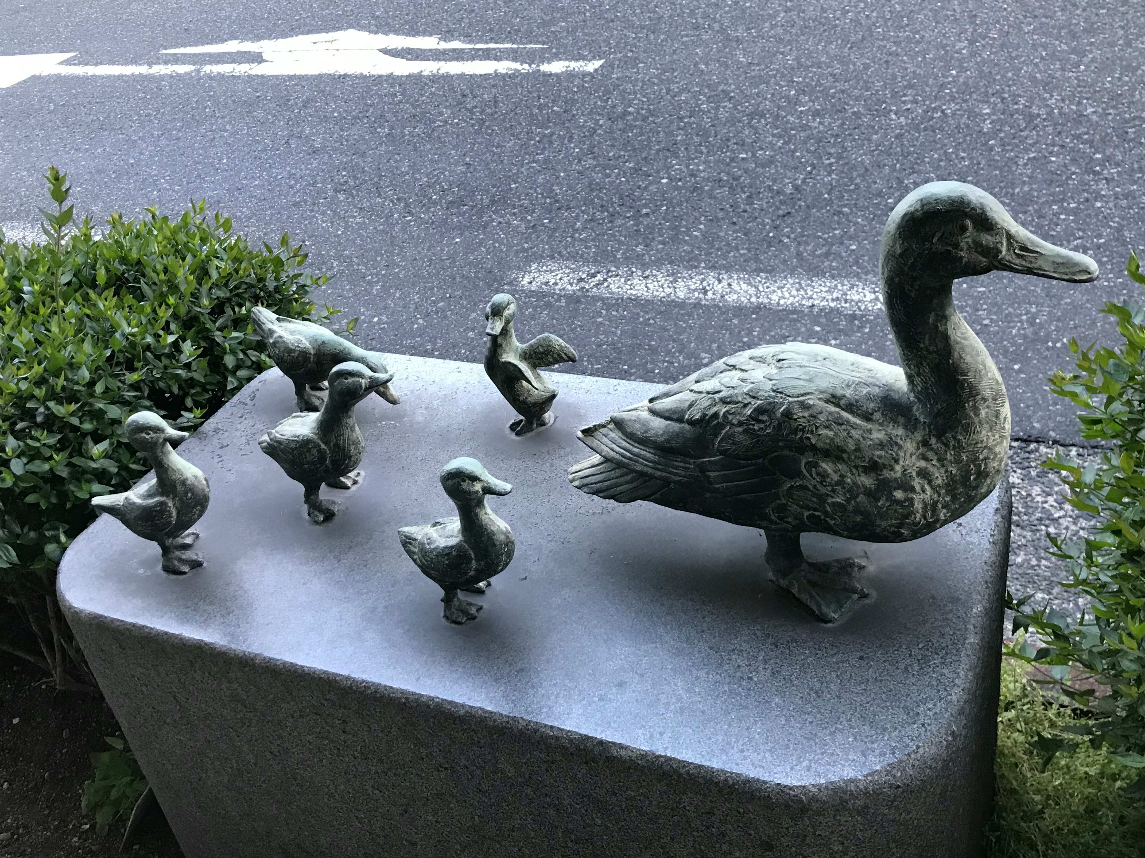 Scultura in bronzo di una madre anatra e dei suoi anatroccoli con fogliame verde sullo sfondo