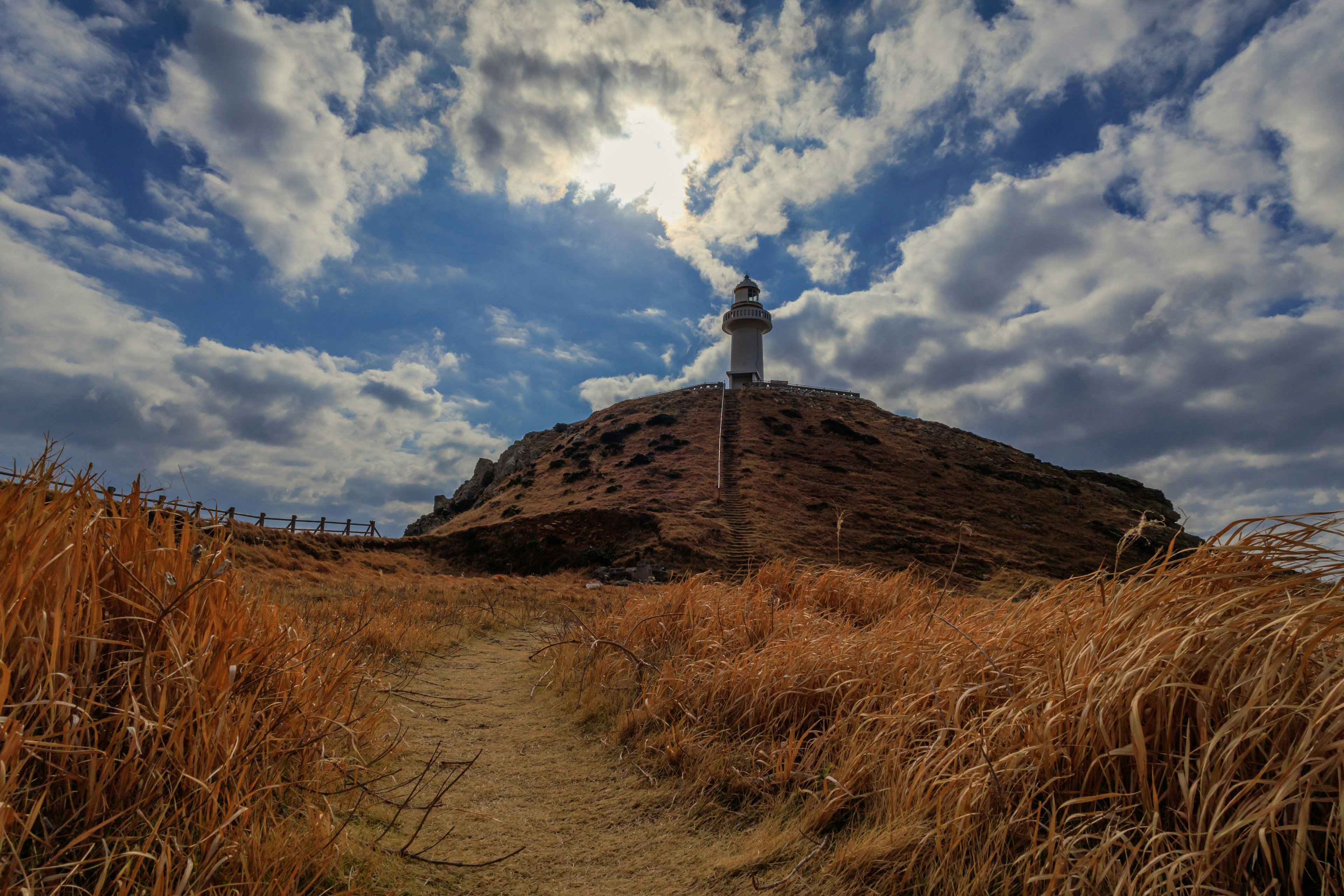 Faro en una colina con un cielo dramático y hierba dorada