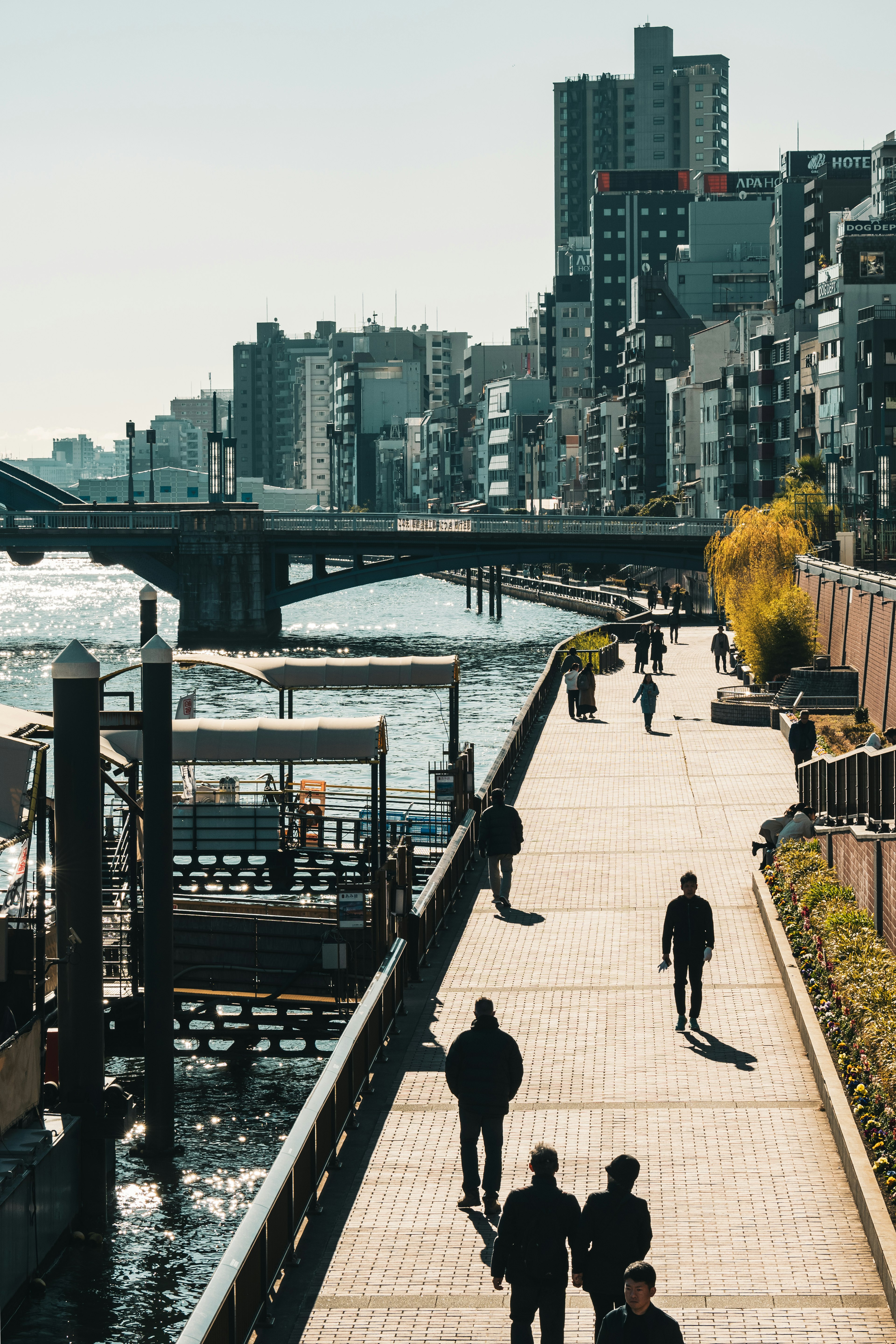 People walking along a riverside promenade with high-rise buildings in the background