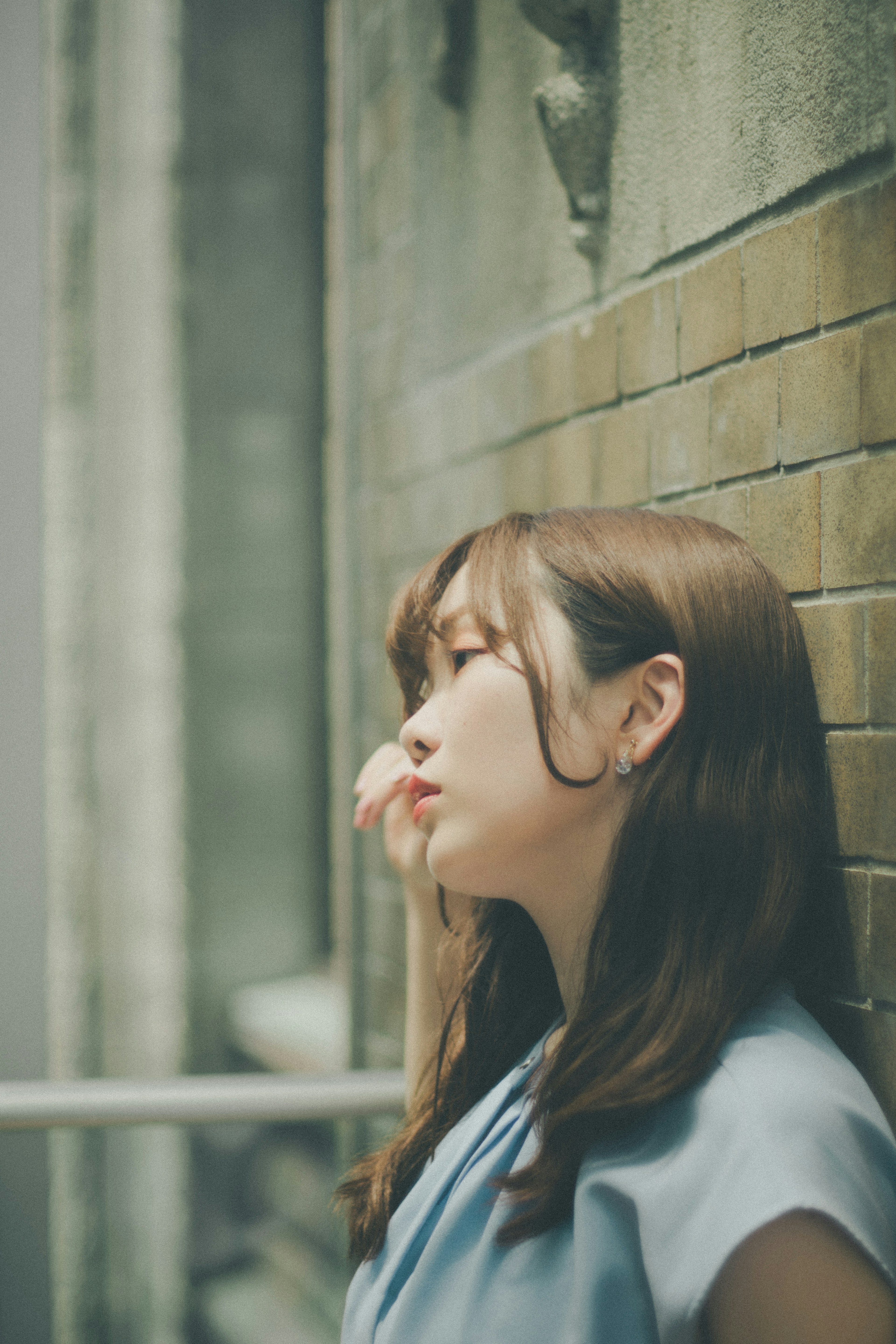 Side profile of a woman leaning against a brick wall wearing a blue outfit