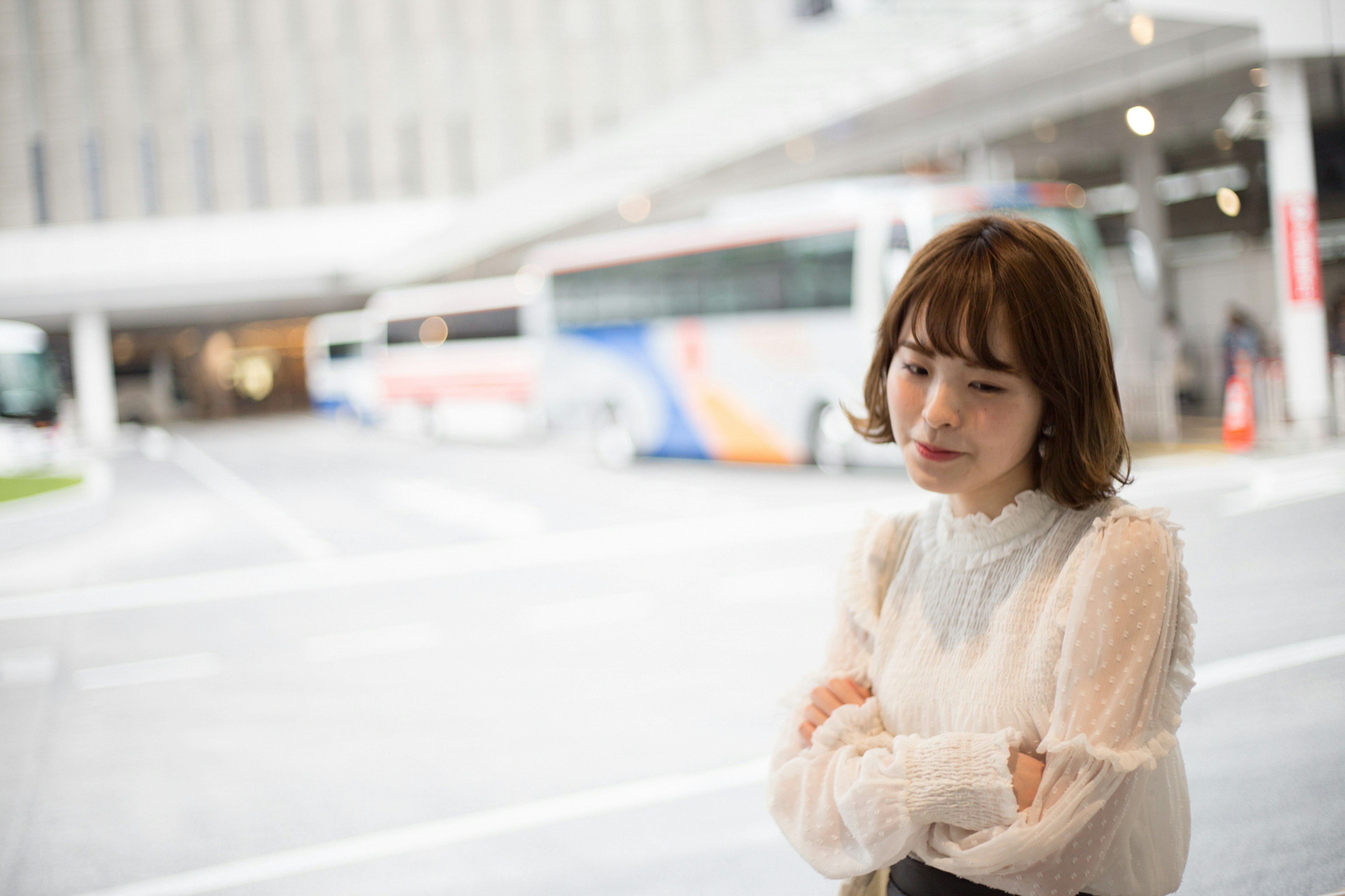 A woman wearing a white blouse standing with crossed arms in front of a bus terminal