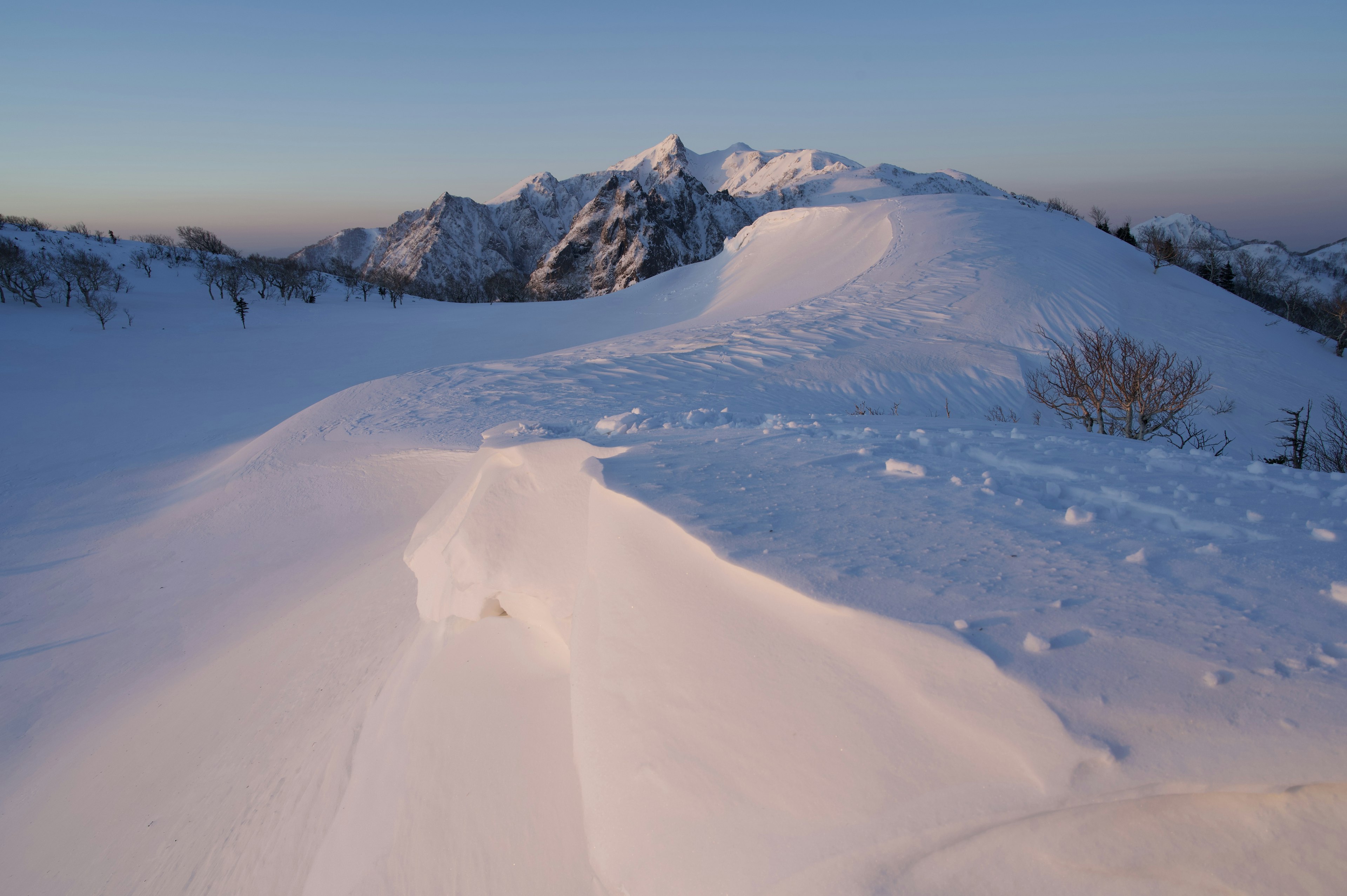 Paisaje montañoso cubierto de nieve con un cielo azul claro y picos distantes