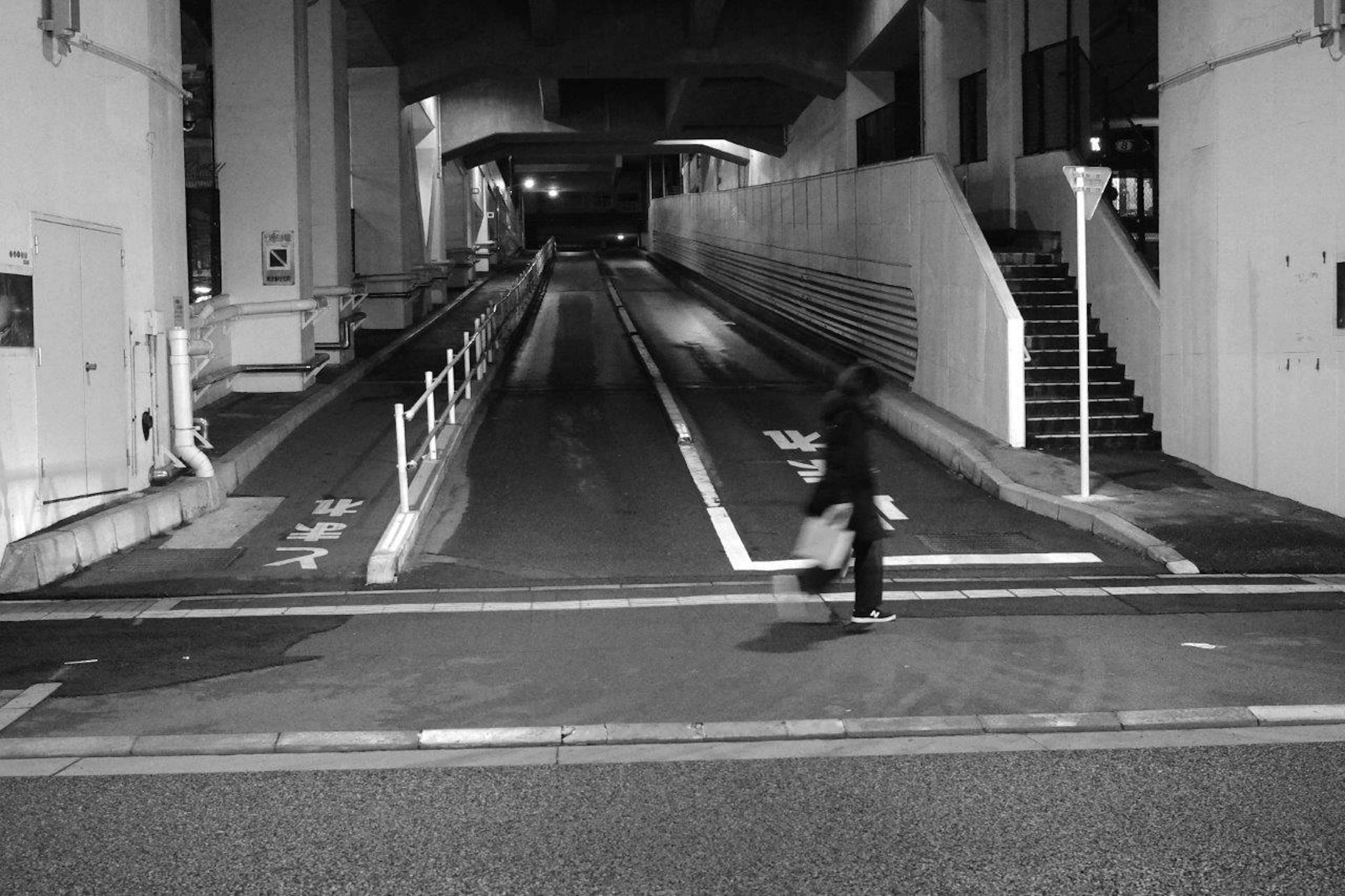 A person crossing a crosswalk in a black and white scene with a dark tunnel in the background