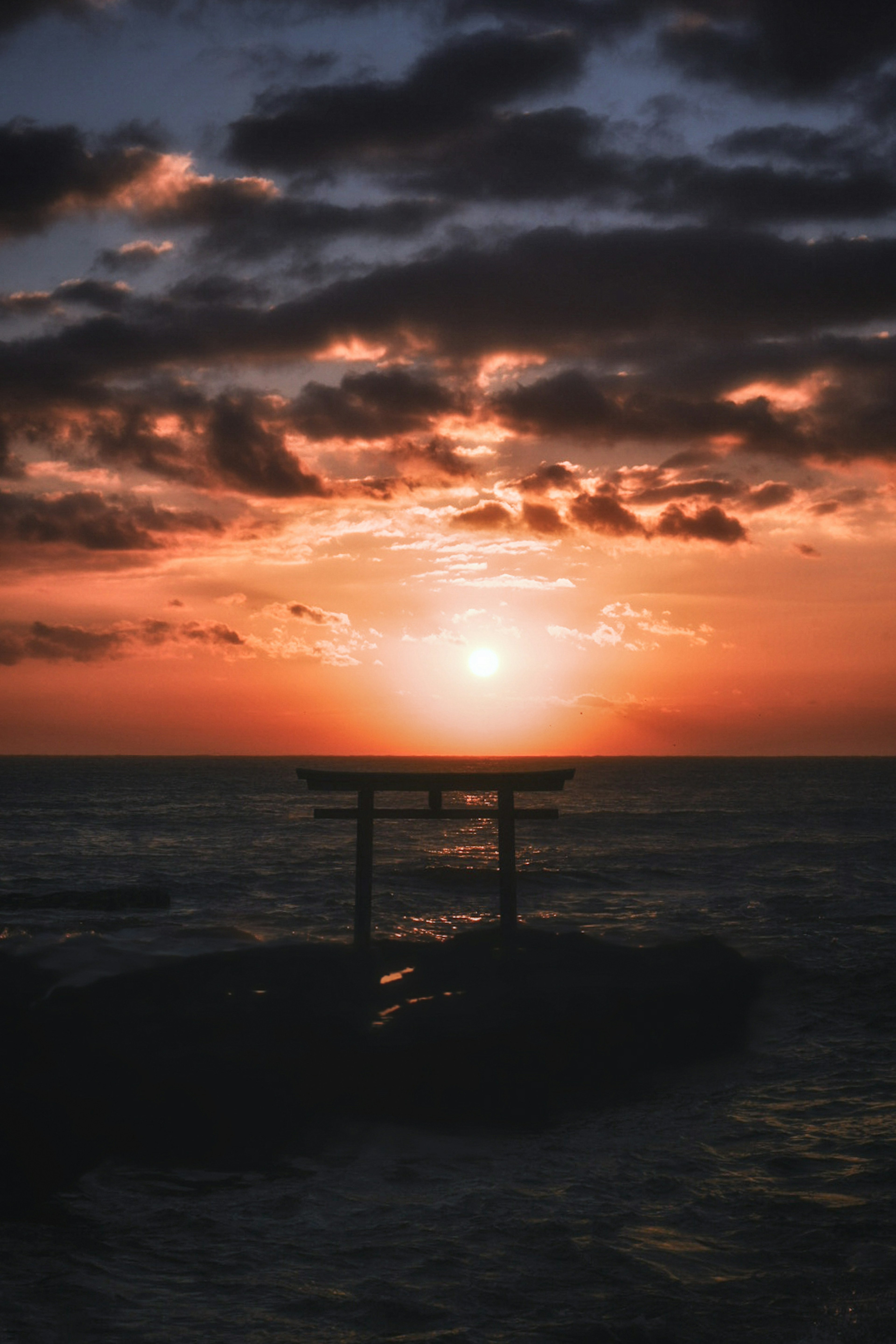 Puerta torii en silueta contra un atardecer sobre el océano