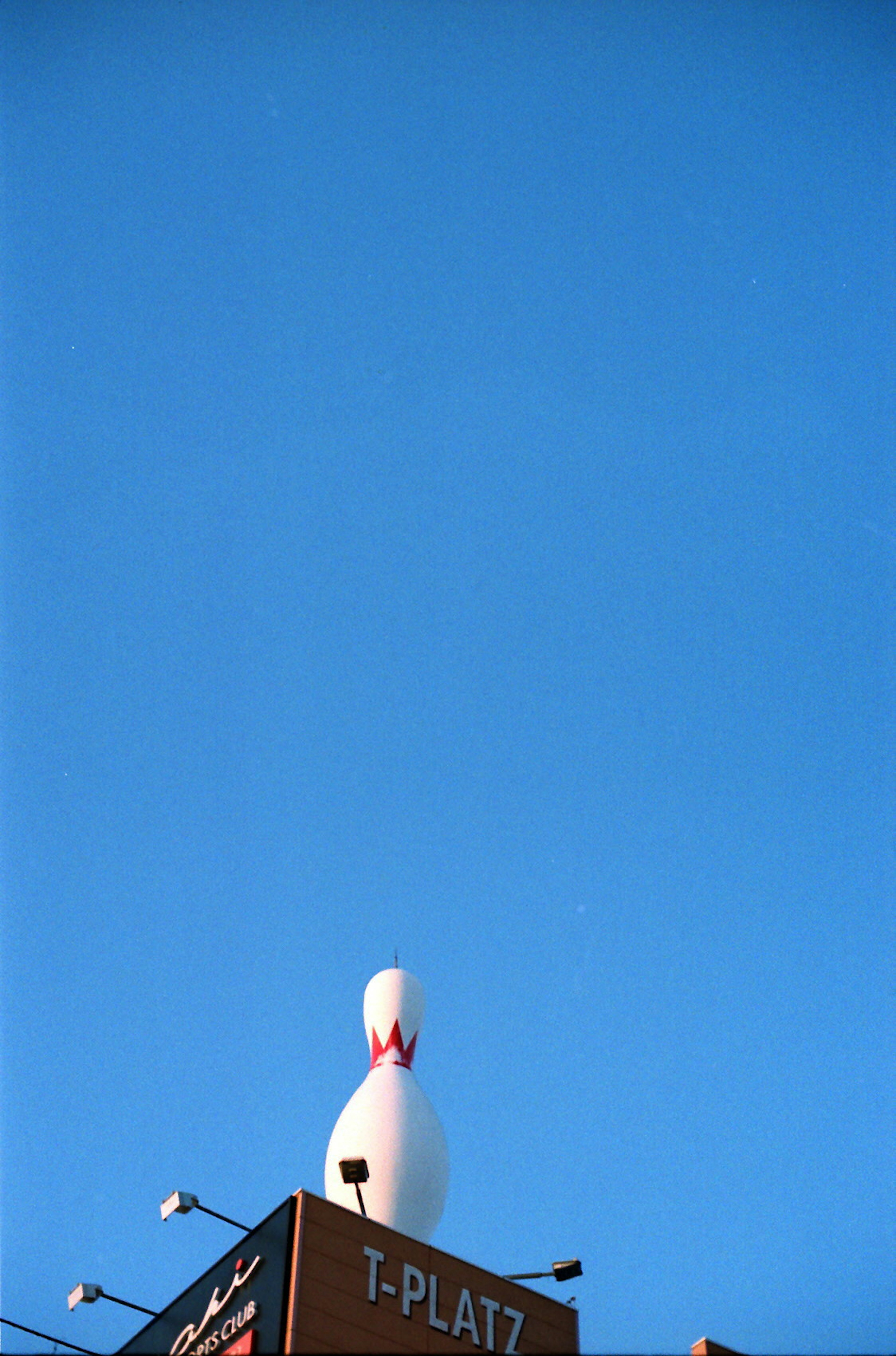 Large bowling pin sign under a clear blue sky T-PLATZ