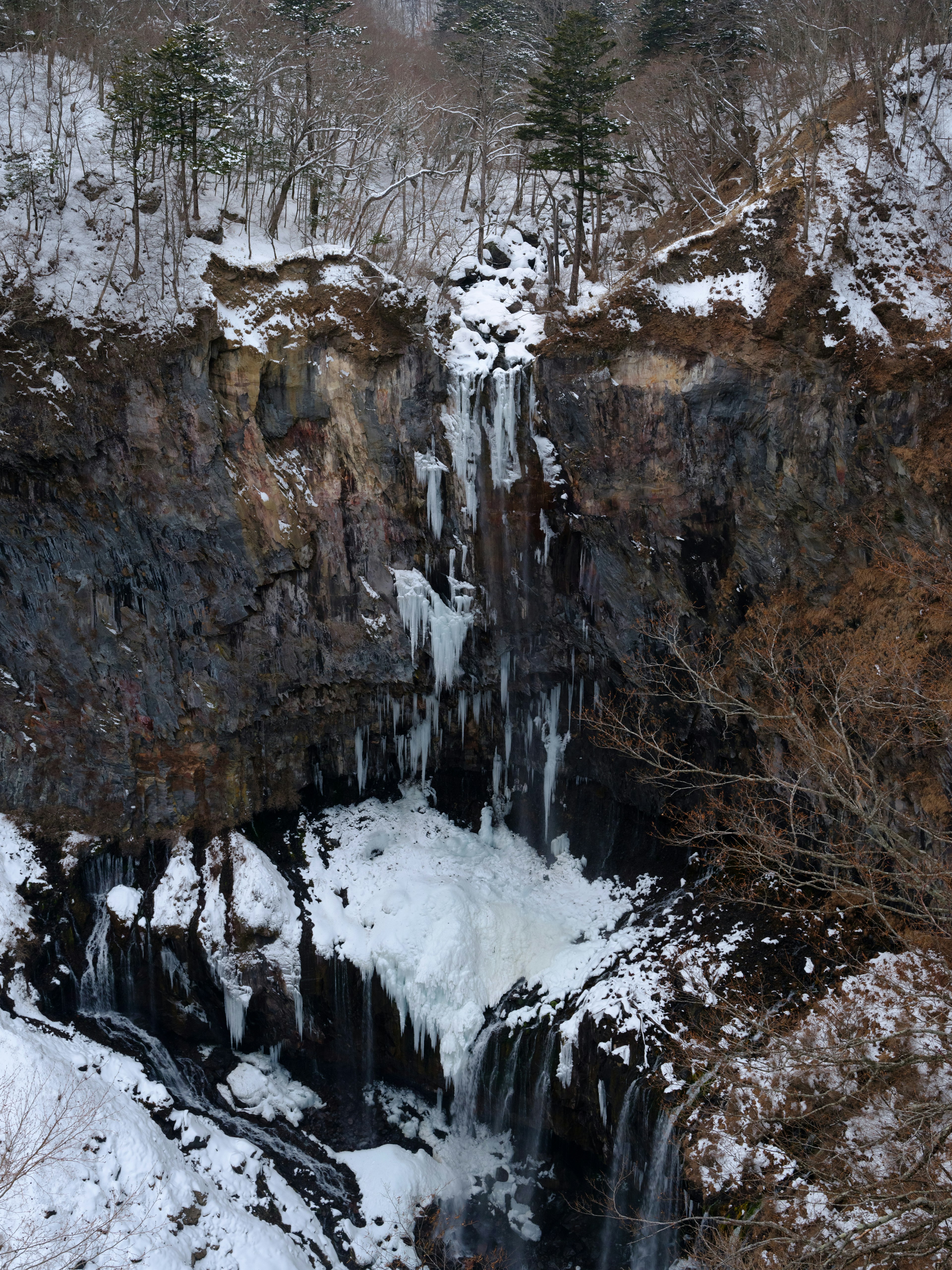 一个冬季景观，瀑布从岩石上倾泻而下，周围环绕着雪