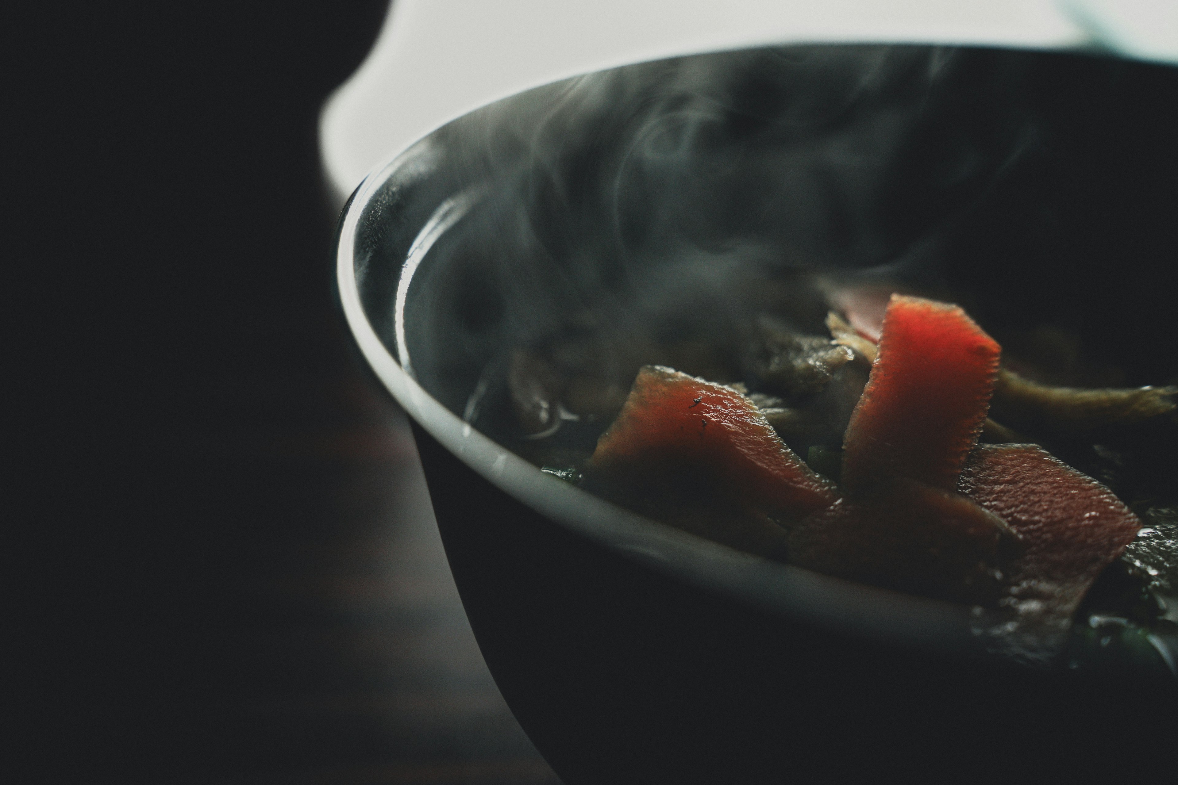 Black bowl with steaming vegetables and chunks of red items