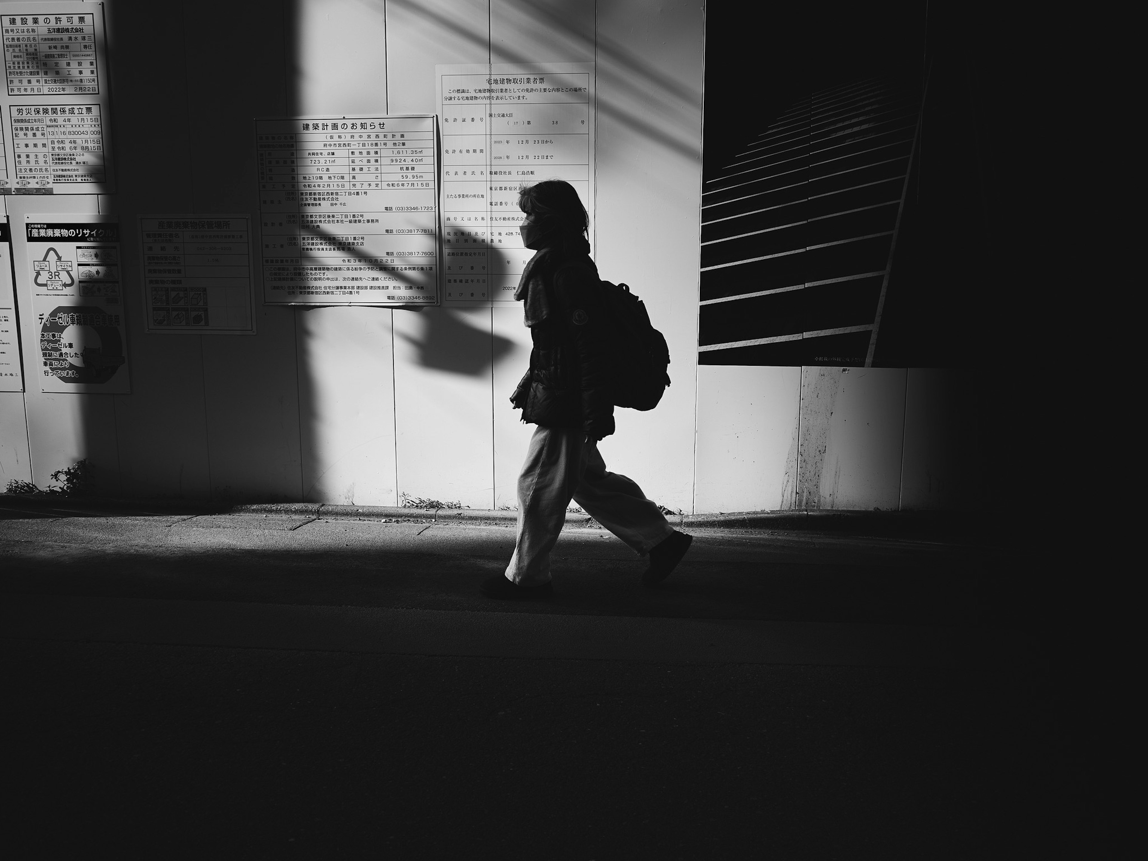 Silhouette of a person walking in shadow against a wall