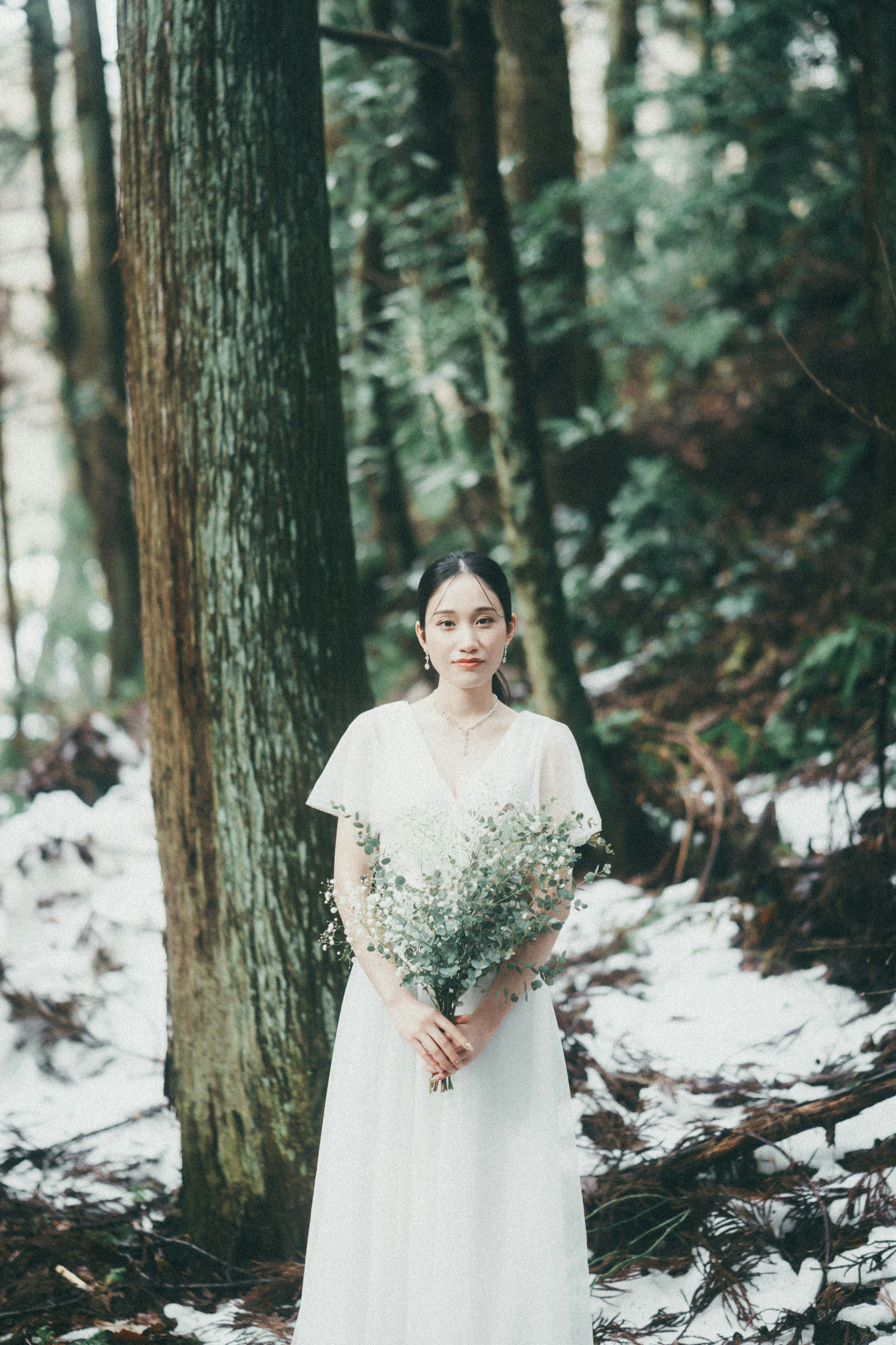 Una mujer con un vestido blanco sosteniendo un ramo de flores en un bosque