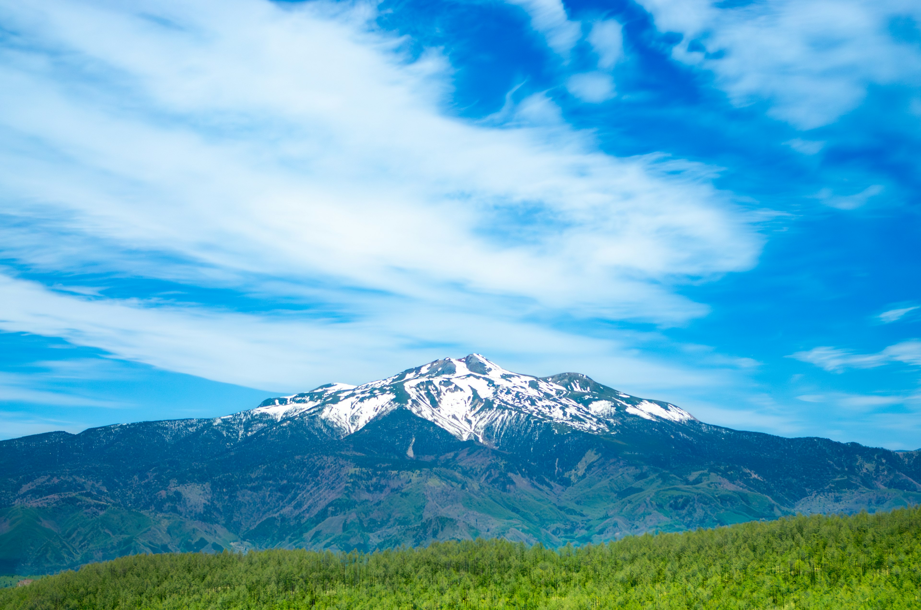 Berglandschaft mit schneebedecktem Gipfel unter blauem Himmel und grünen Hügeln im Vordergrund