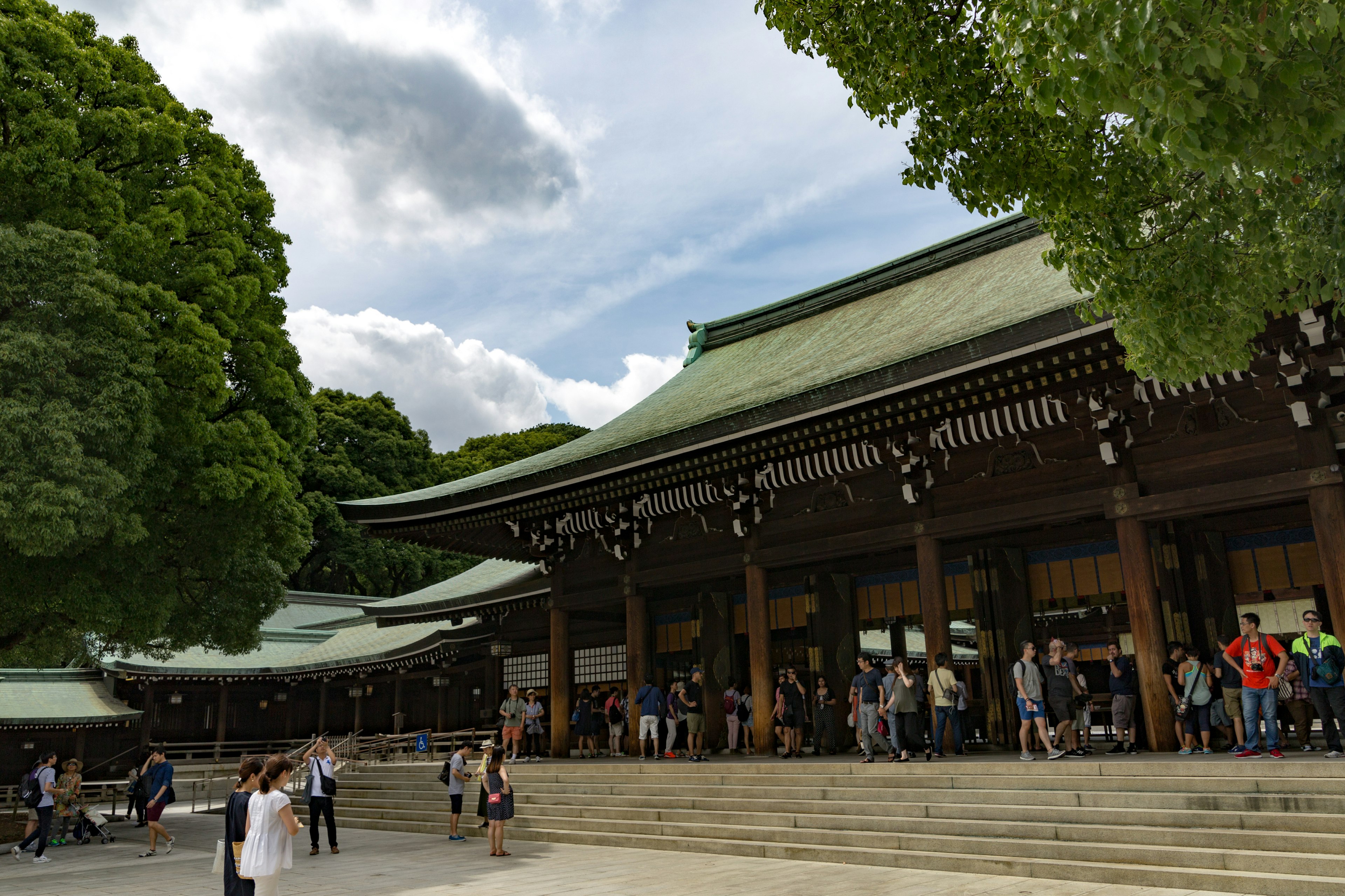 Visitatori riuniti all'ingresso del Santuario Meiji circondato da una vegetazione lussureggiante e da una bella architettura