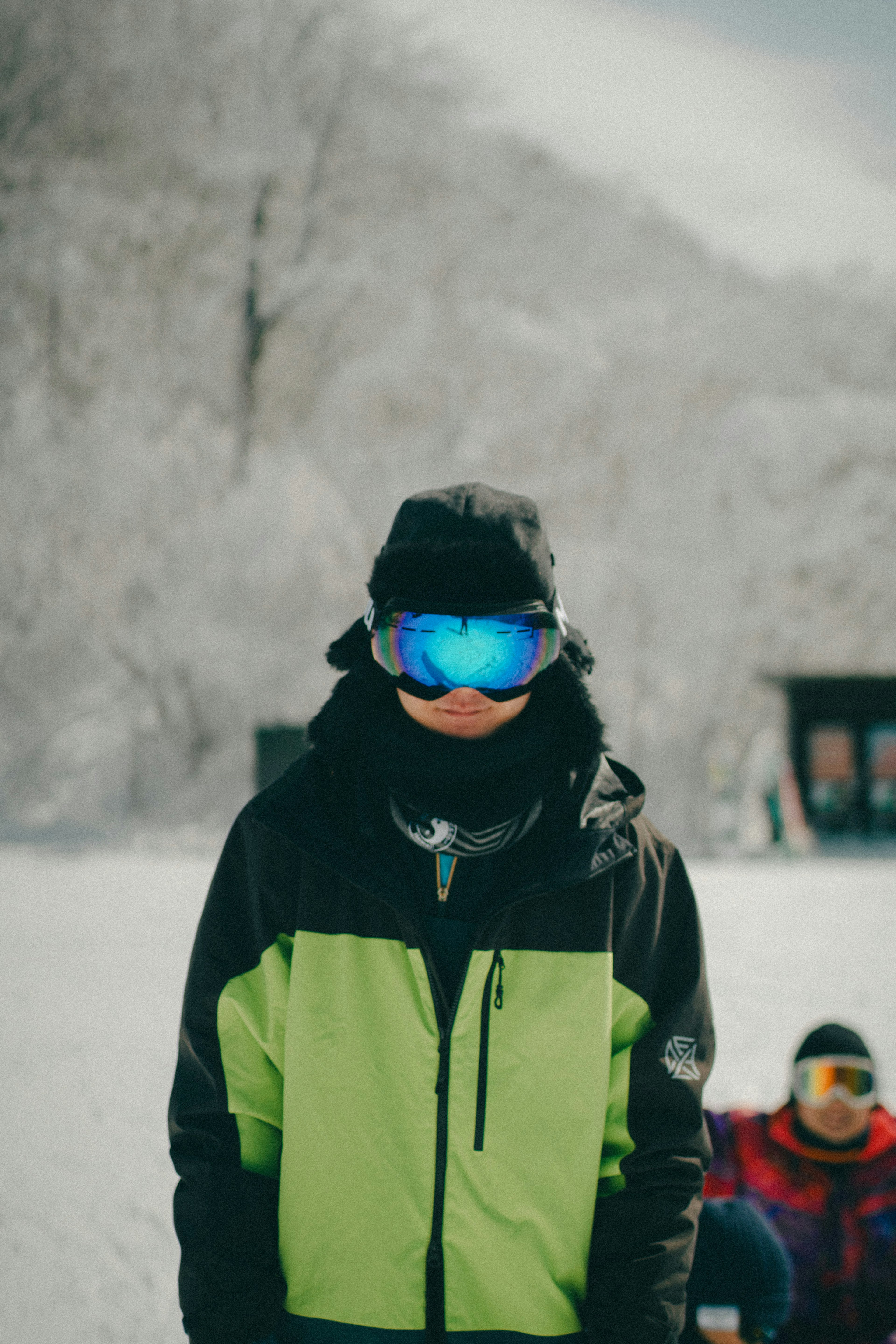 在雪景中站着的人，穿着绿色和黑色的夹克，戴着蓝色护目镜